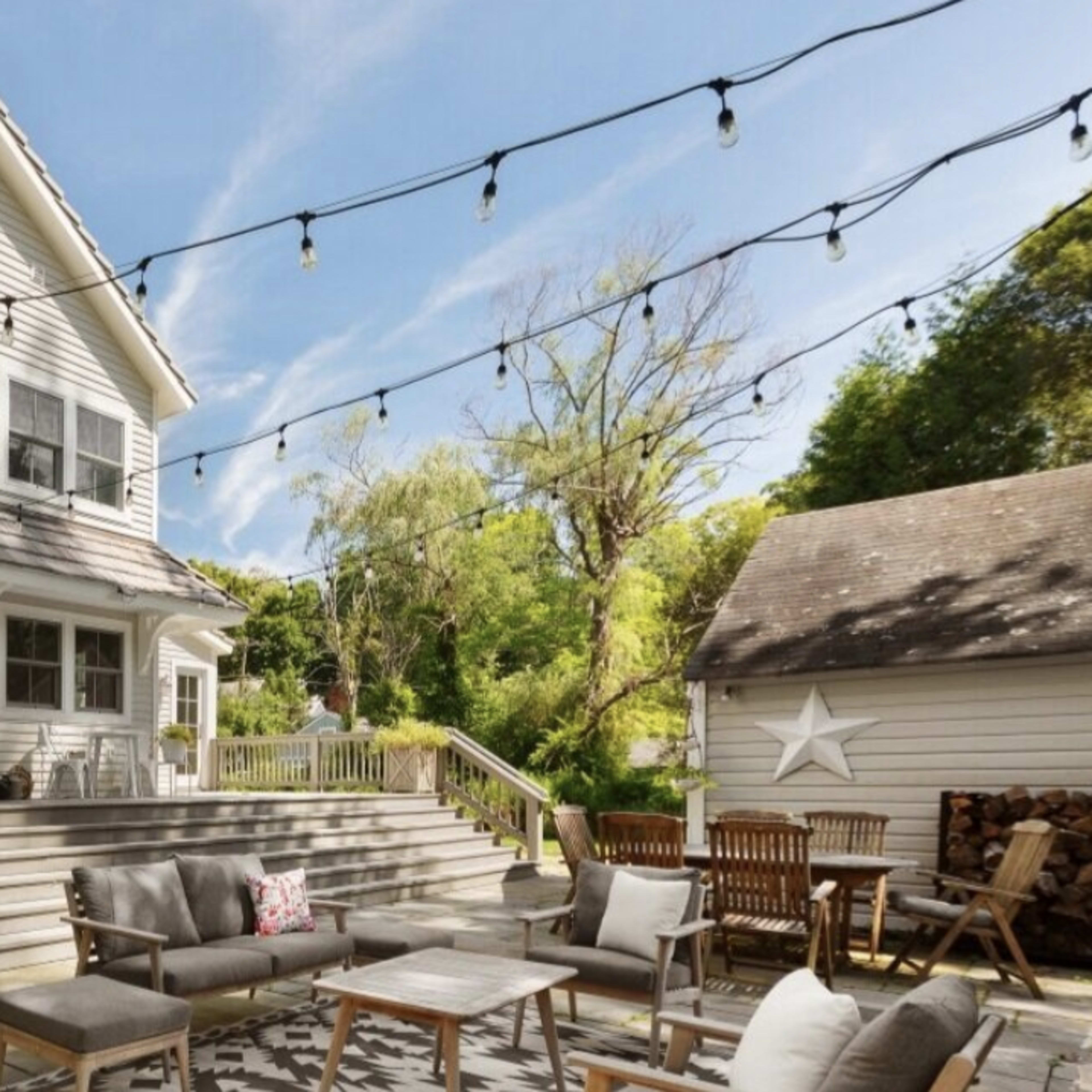 A two-story house with a deck, outdoor seating, and string lights overhead.