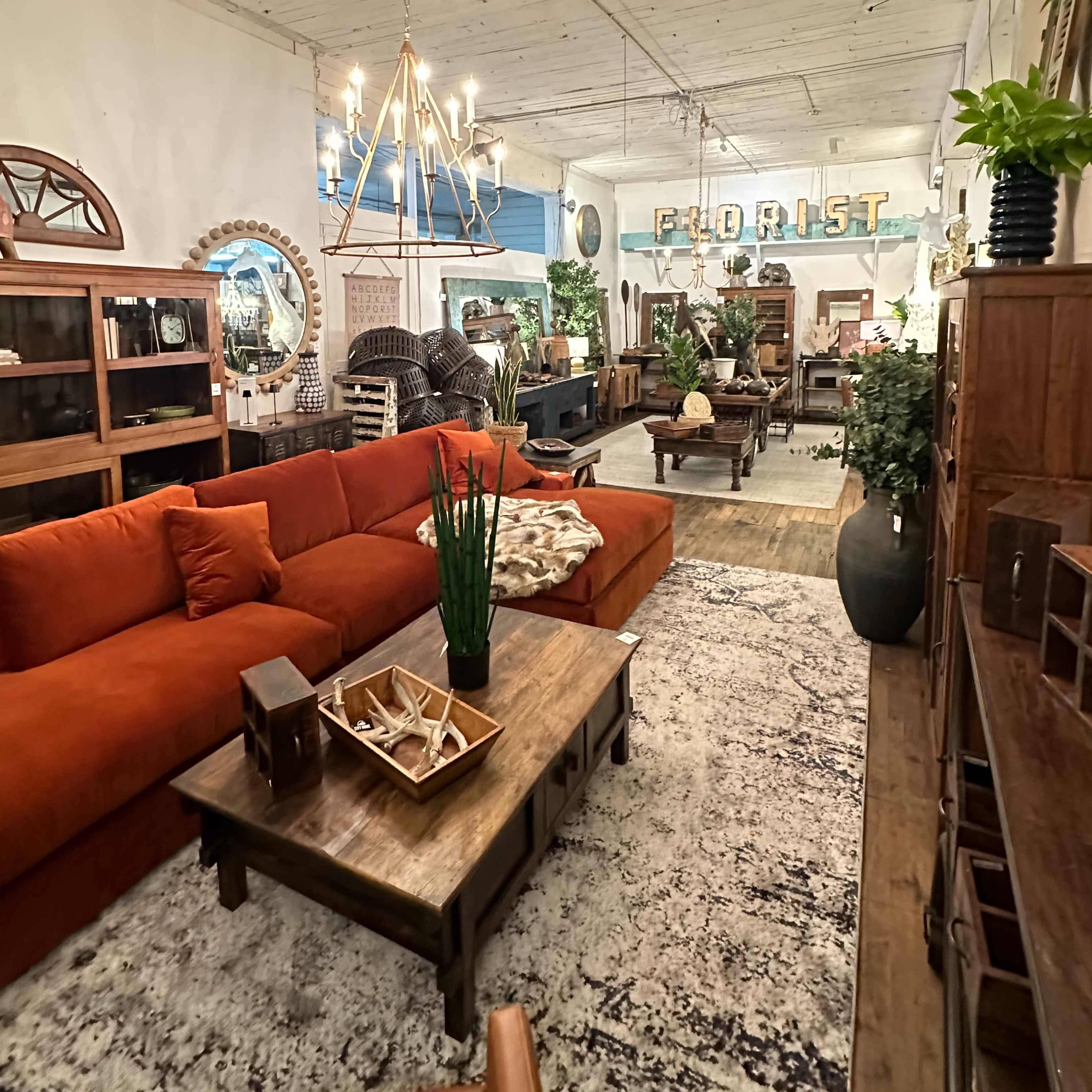 A spacious interior of a floral shop featuring a large orange sofa, wooden furniture, and various plants throughout the room.