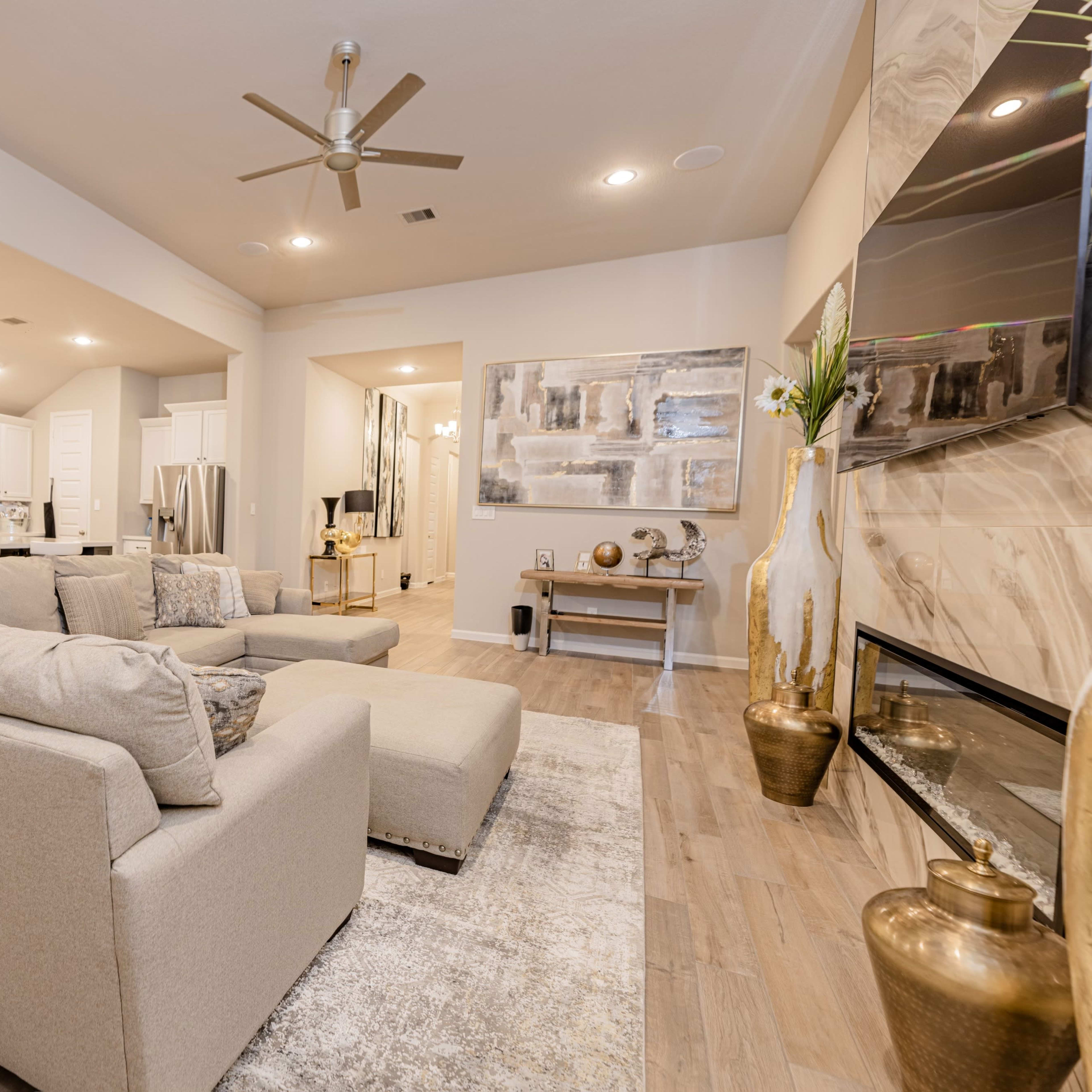 A modern living room features a large sectional sofa, a fireplace, and an open layout leading to a kitchen.
