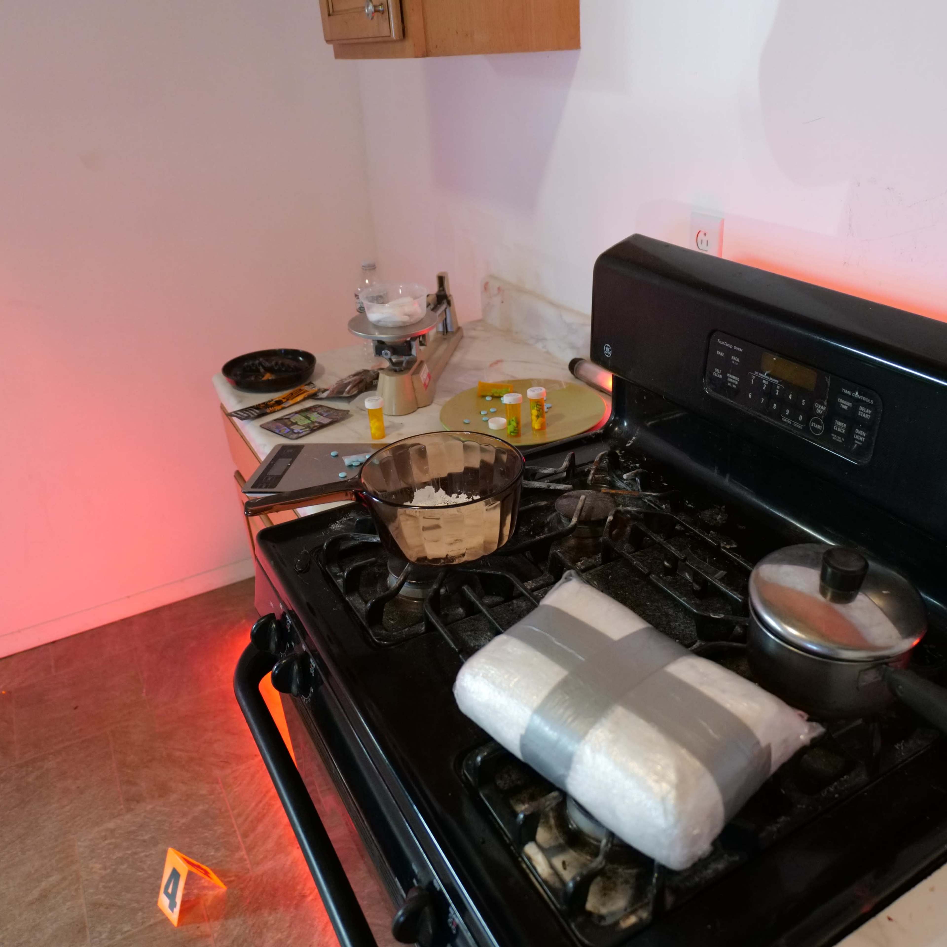 A black stove with a pot and a bowl on it sits next to various kitchen items on a countertop, illuminated by red lighting.