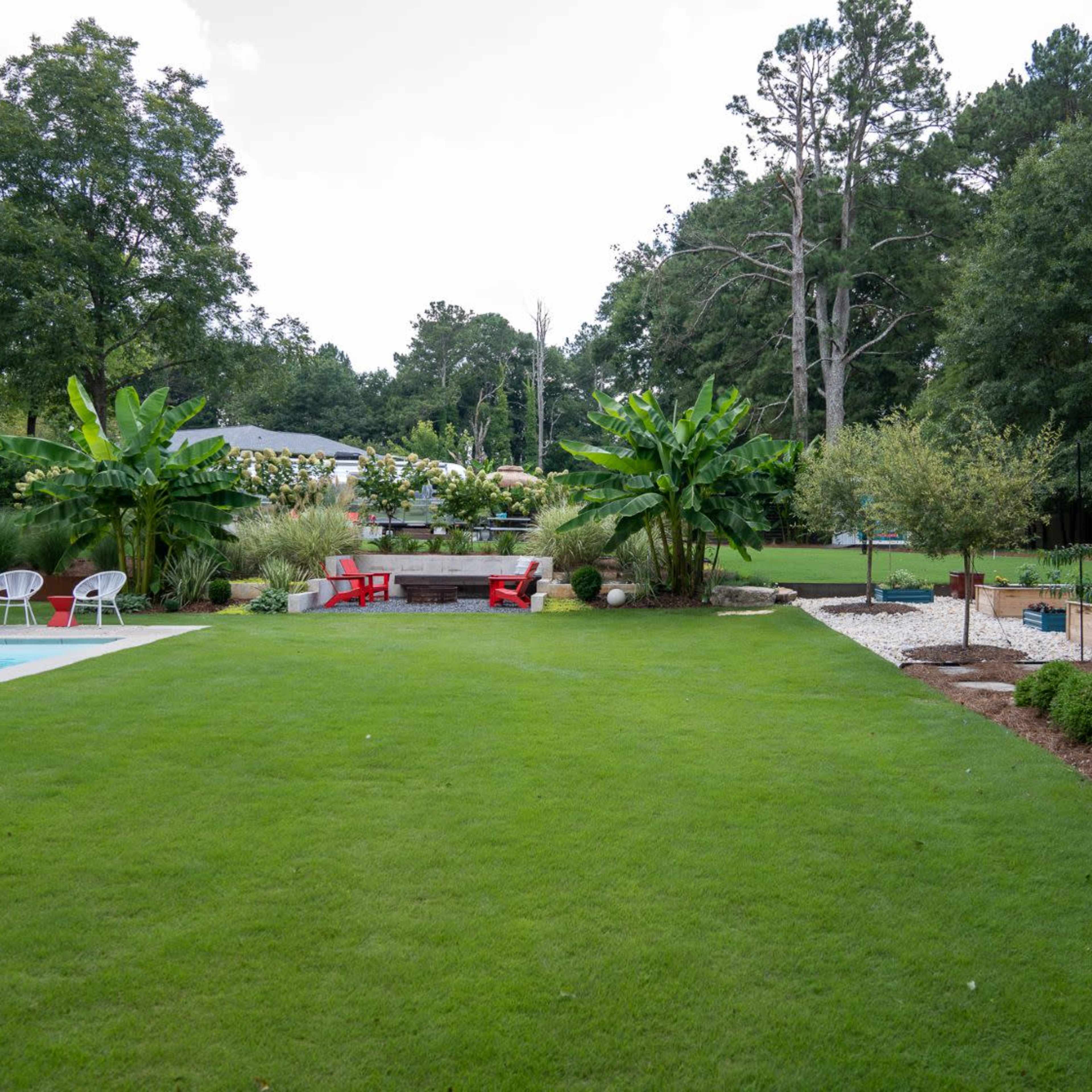 A well-maintained backyard featuring a swimming pool, curated plant beds, and seating areas surrounded by lush greenery.