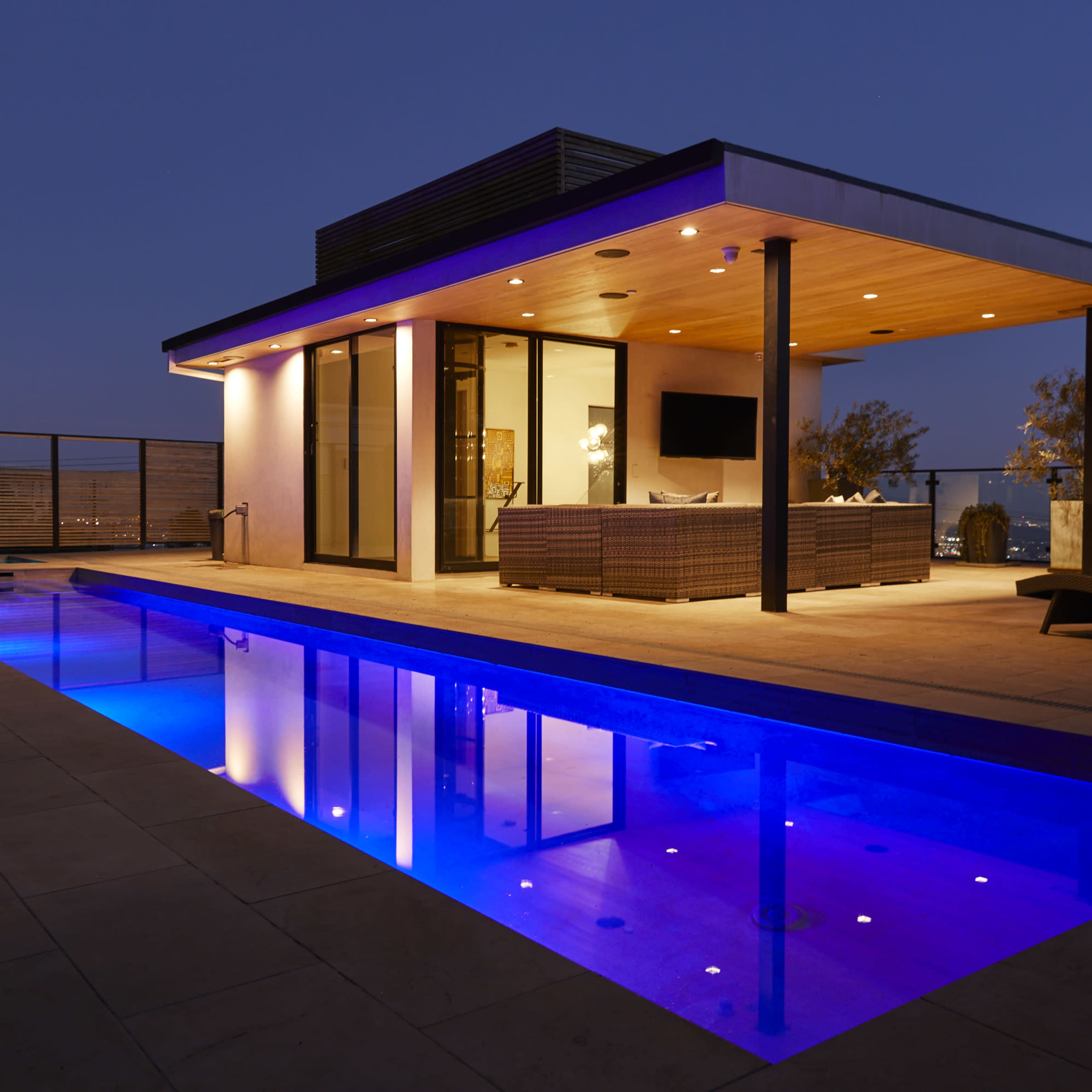 A modern building features a pool illuminated with blue lights, reflecting its contemporary architecture against a twilight sky.