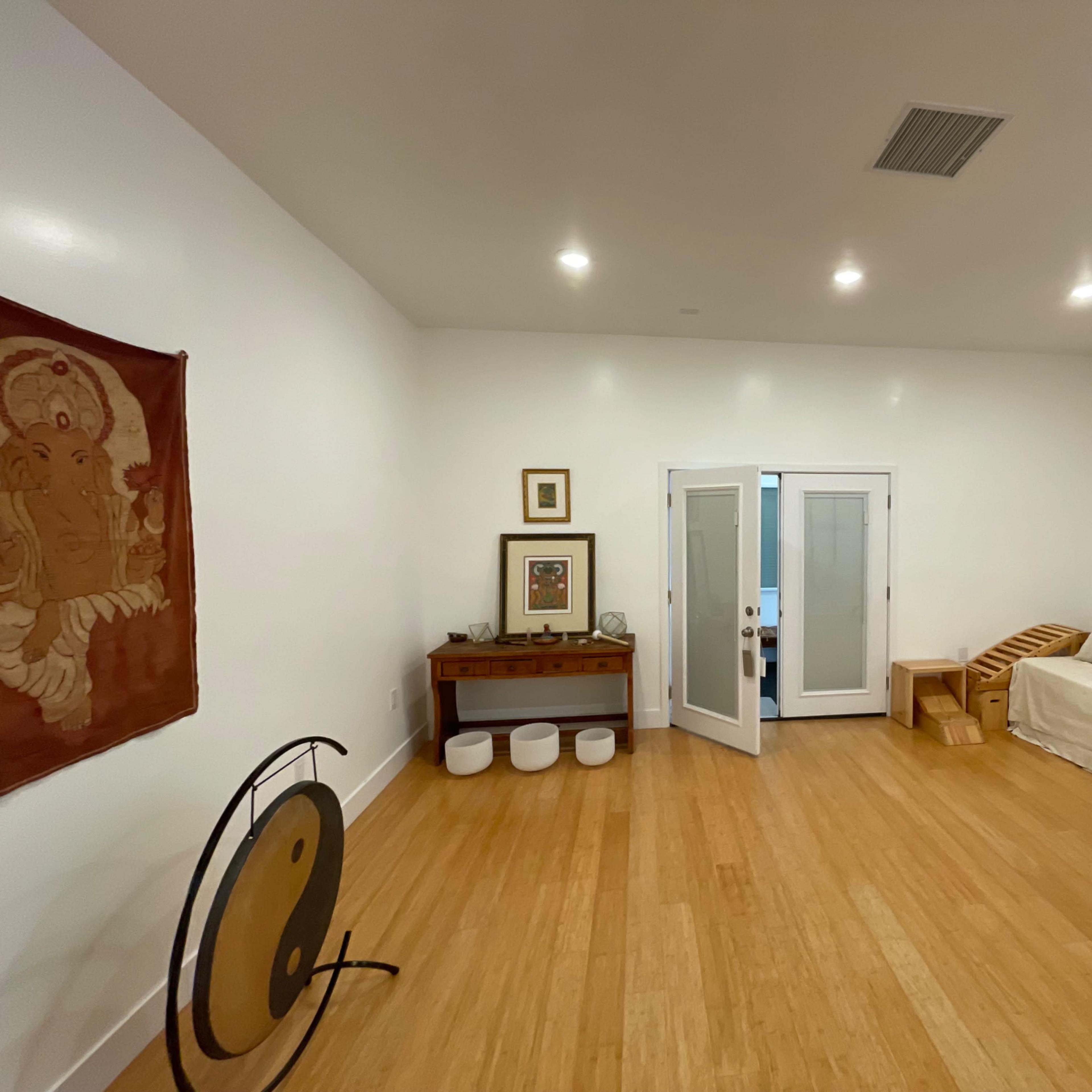 A spacious, brightly lit room with bamboo flooring, featuring a large sofa, a wooden table, and several decorative items along the walls.