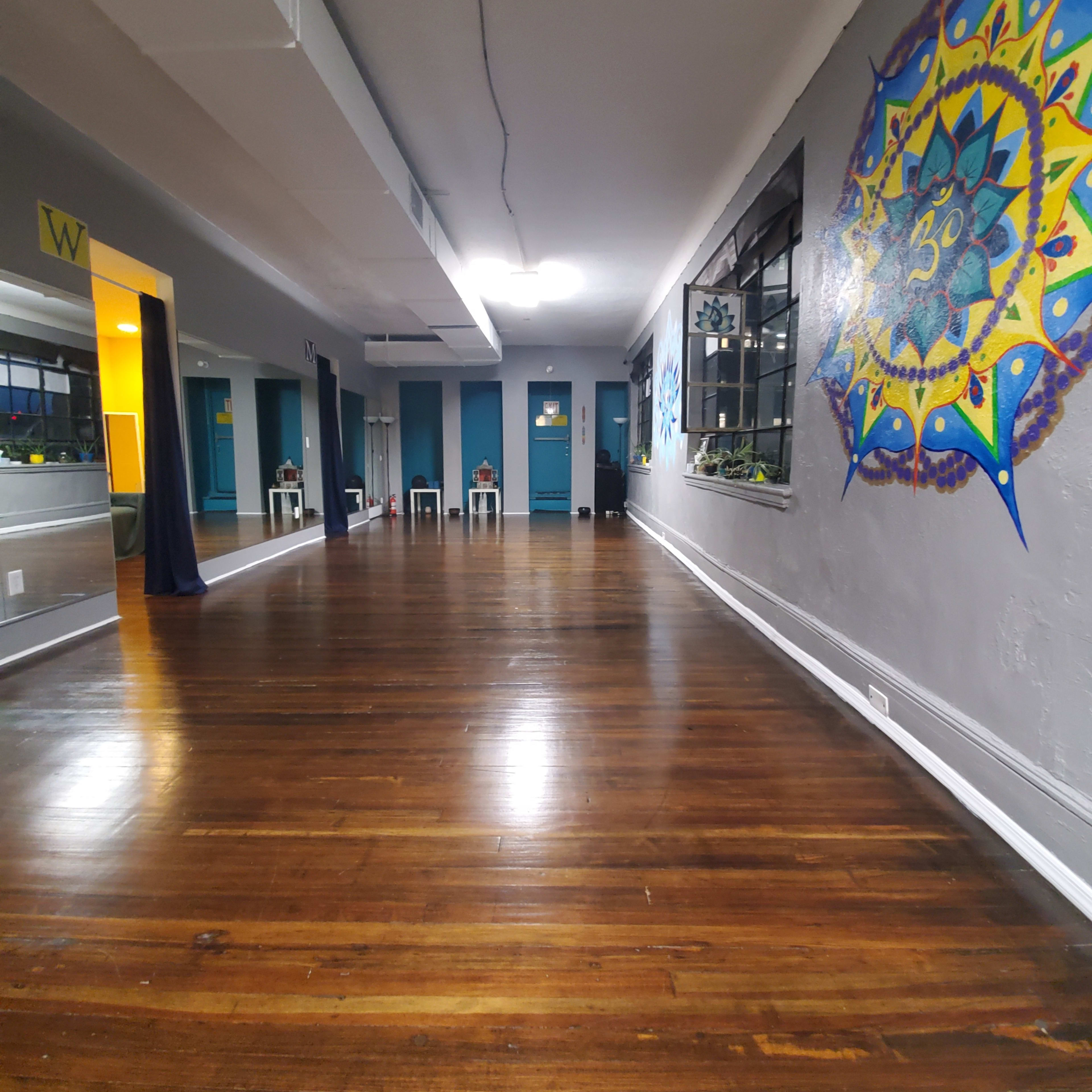 An empty dance studio with polished wooden floors and blue walls adorned with colorful artwork.