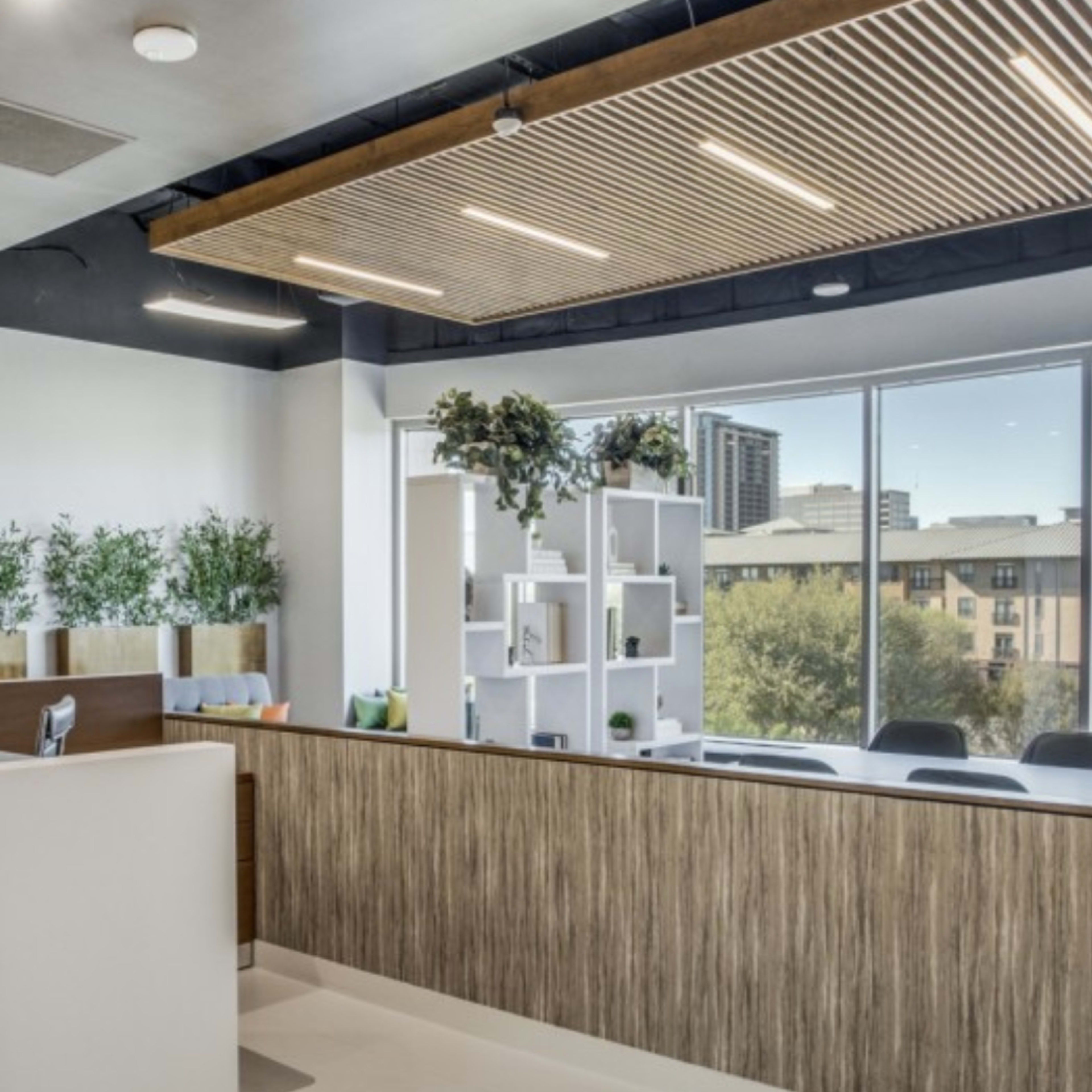 A modern reception area with a wooden desk, seating, and large windows overlooking a cityscape.