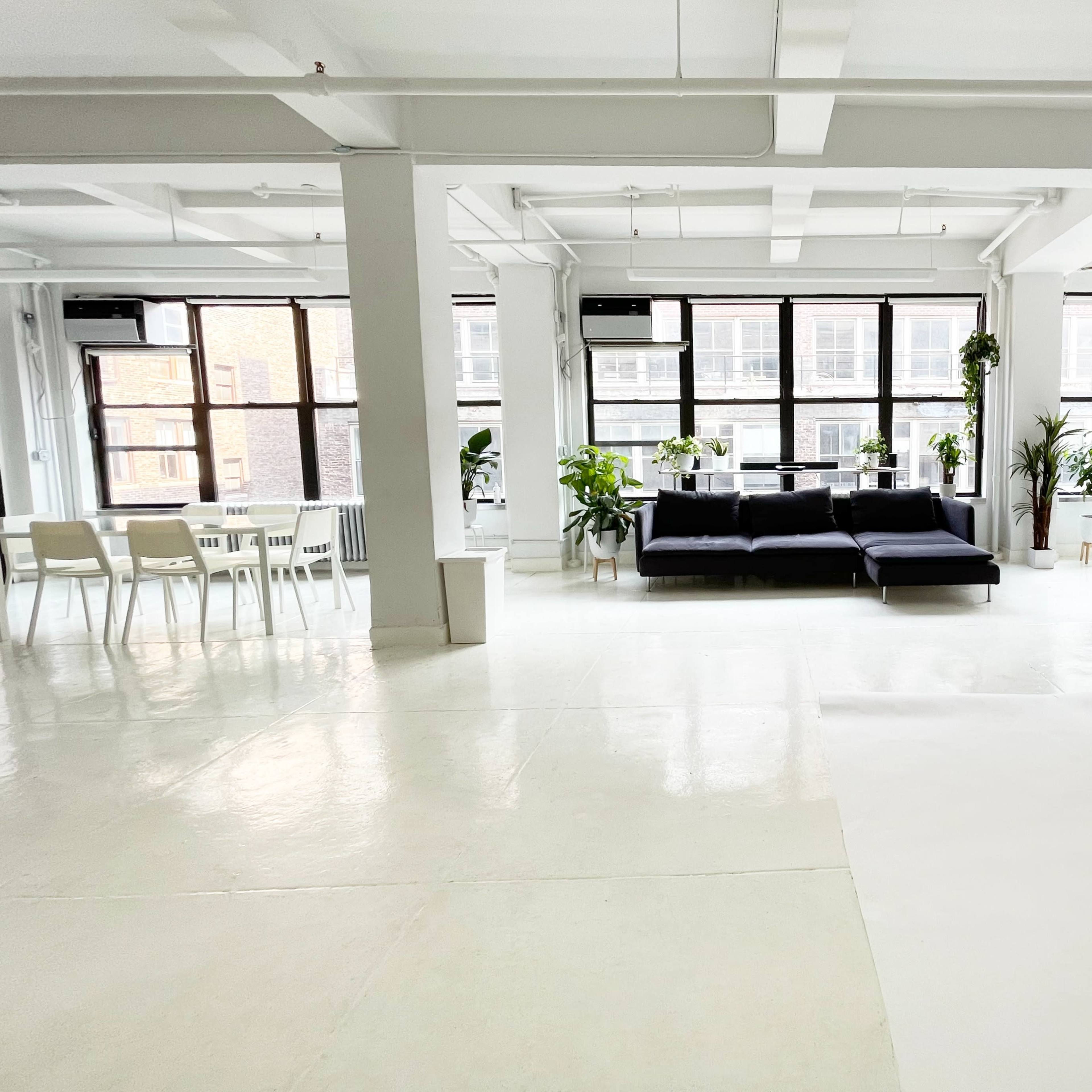 A spacious studio with large windows, a black sofa, and a white backdrop.