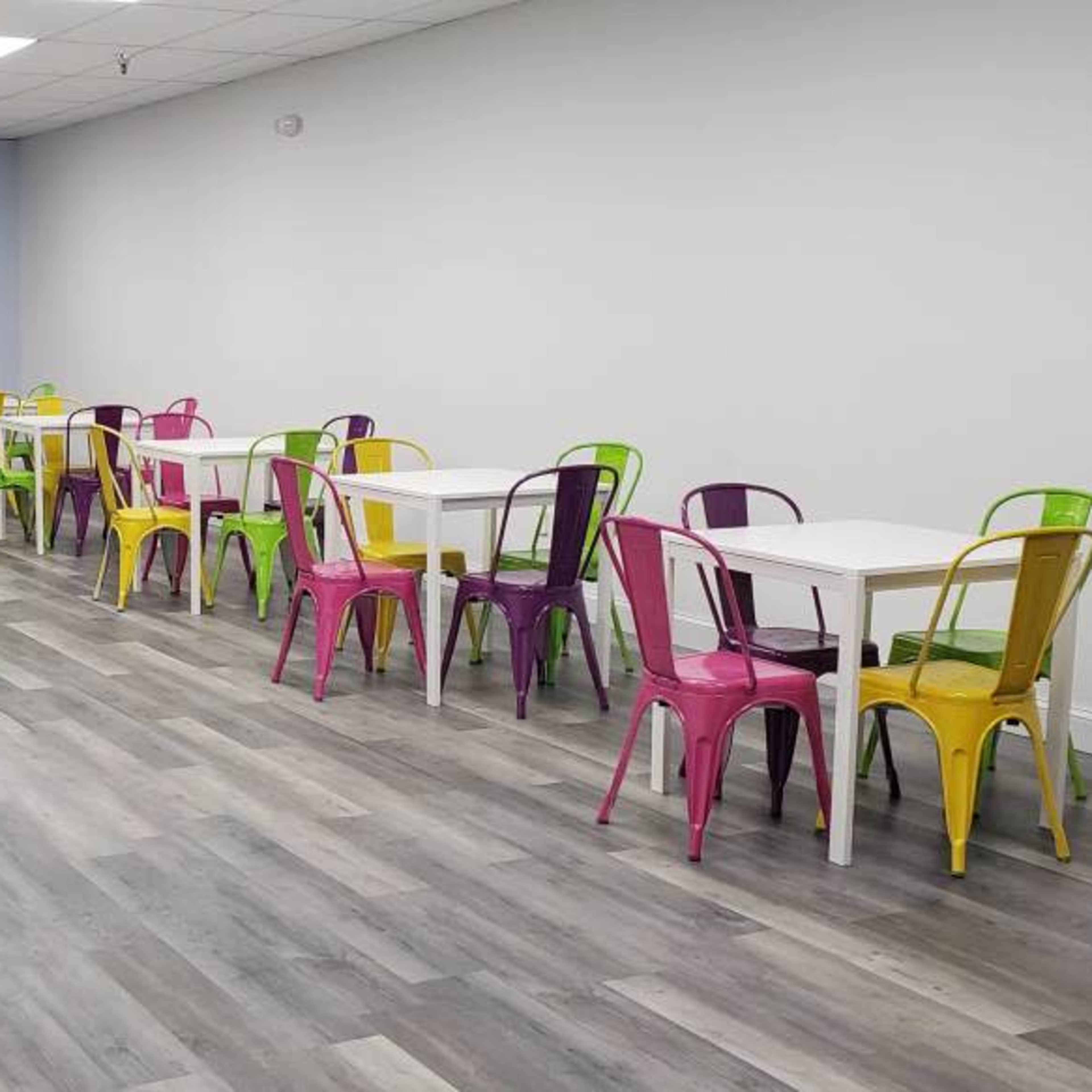 A modern snack area with colorful metal chairs and tables arranged neatly on a gray wooden floor.