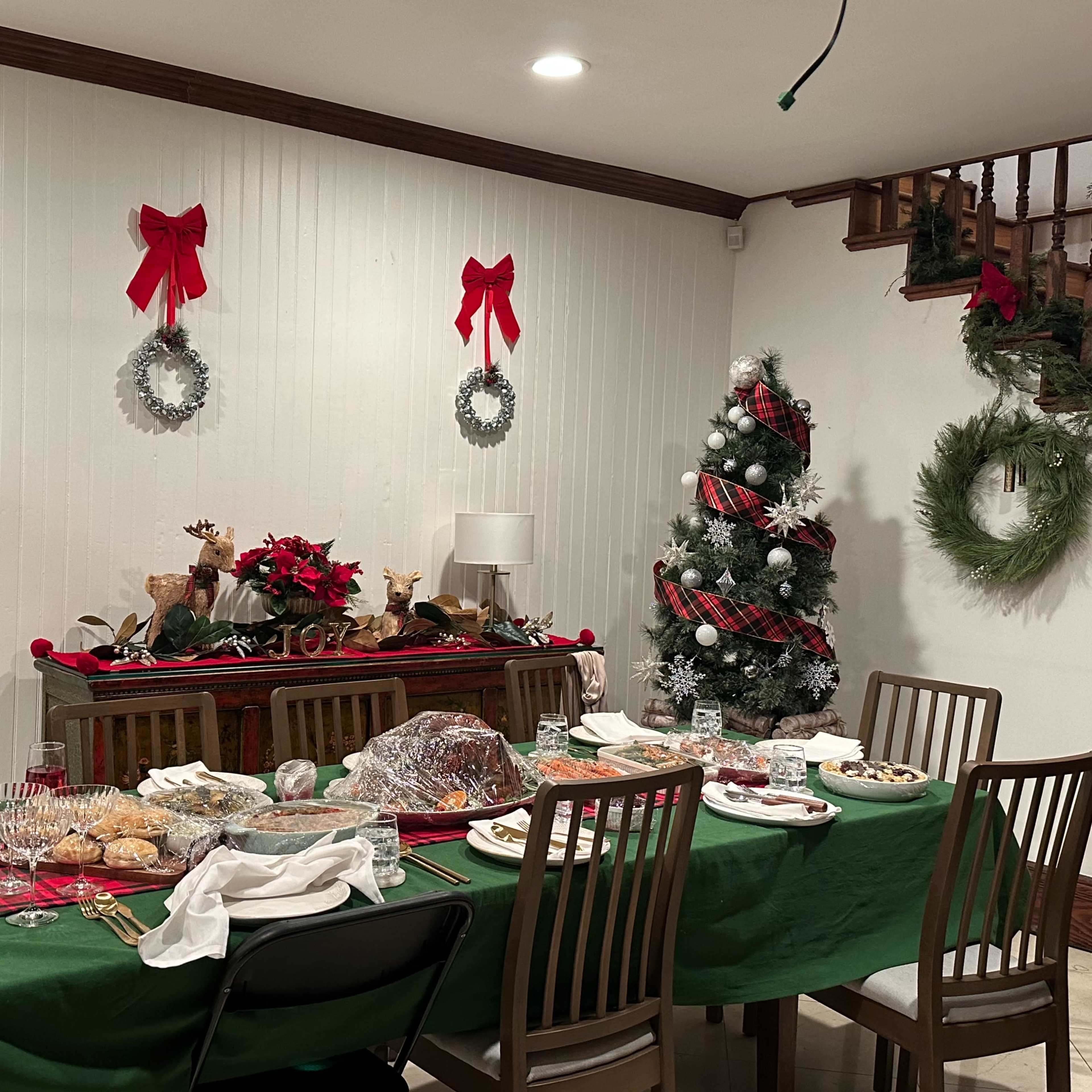 A dining table set with food and decorated for a holiday celebration is positioned in a room adorned with festive garlands, wreaths, and red bows.