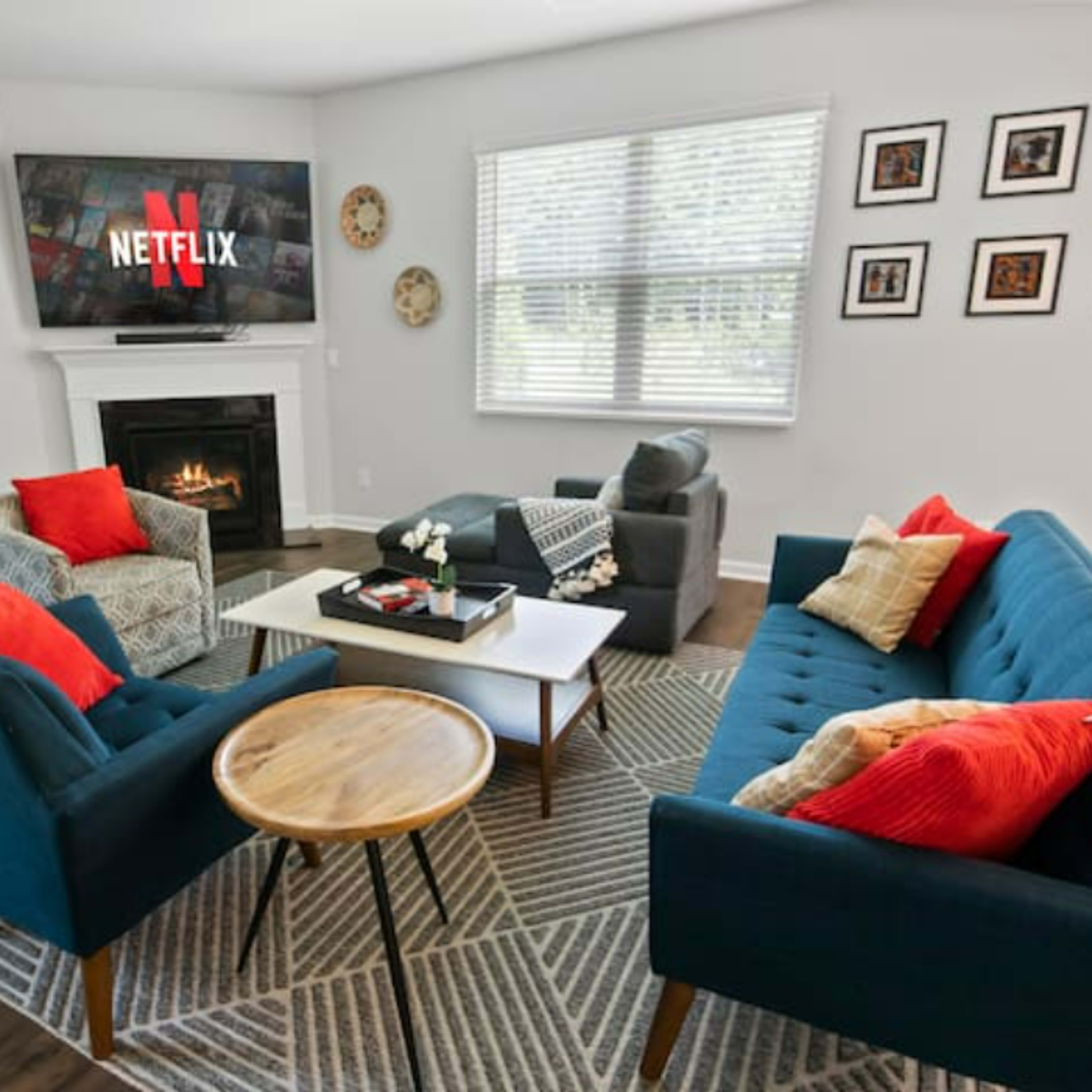 The living room features a fireplace, a large TV displaying the Netflix logo, and blue sofas arranged around a coffee table with decorative accents.