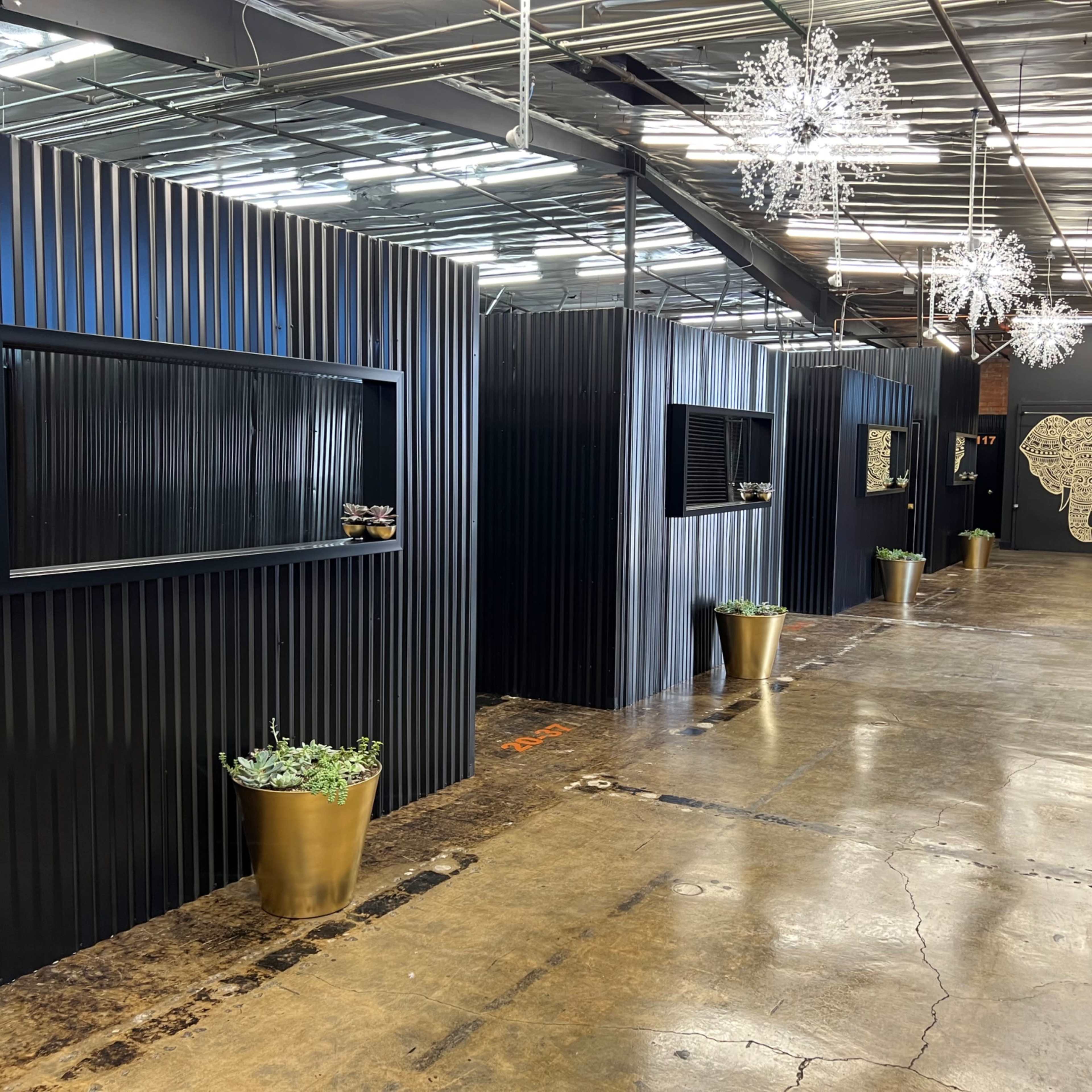 A modern indoor space with black corrugated walls, decorative mirrors, potted plants, and a whimsical elephant mural at the far end.