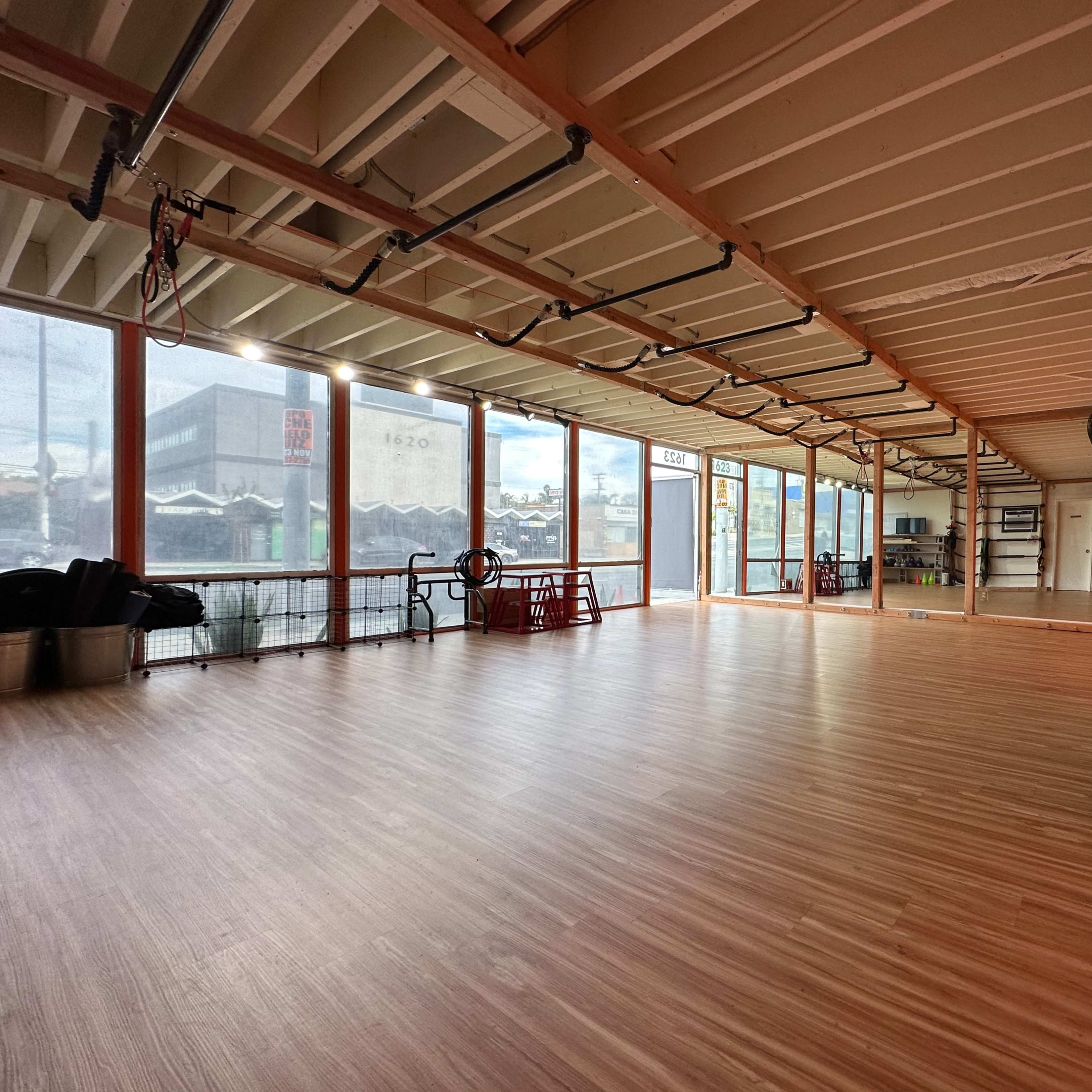 A spacious interior room with wooden flooring and large windows overlooking a cityscape.