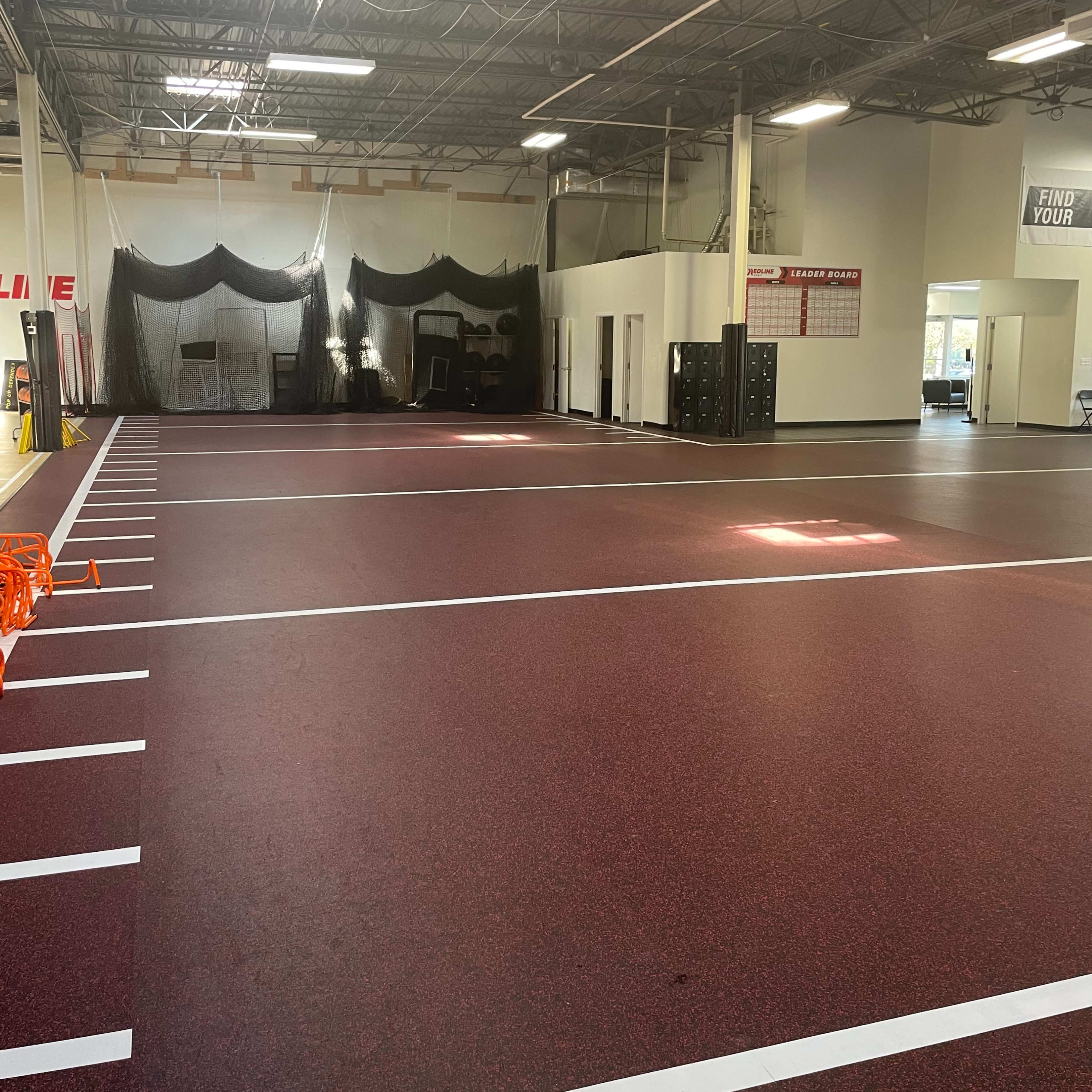 A spacious indoor training facility with a rubberized red floor and marked lanes, illuminated by overhead lights.