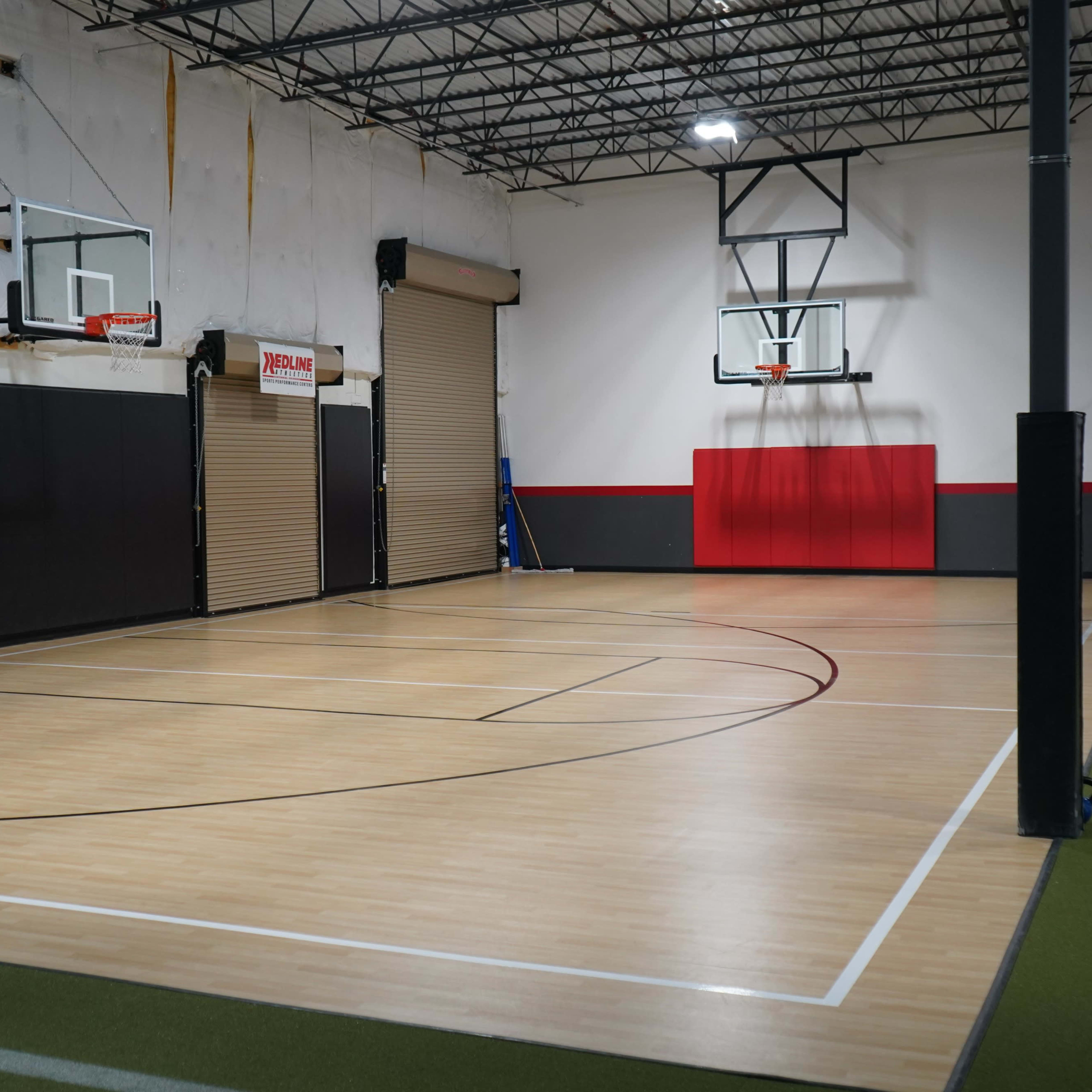 An indoor basketball court with two basketball hoops at opposite ends and a section of green turf to the right.
