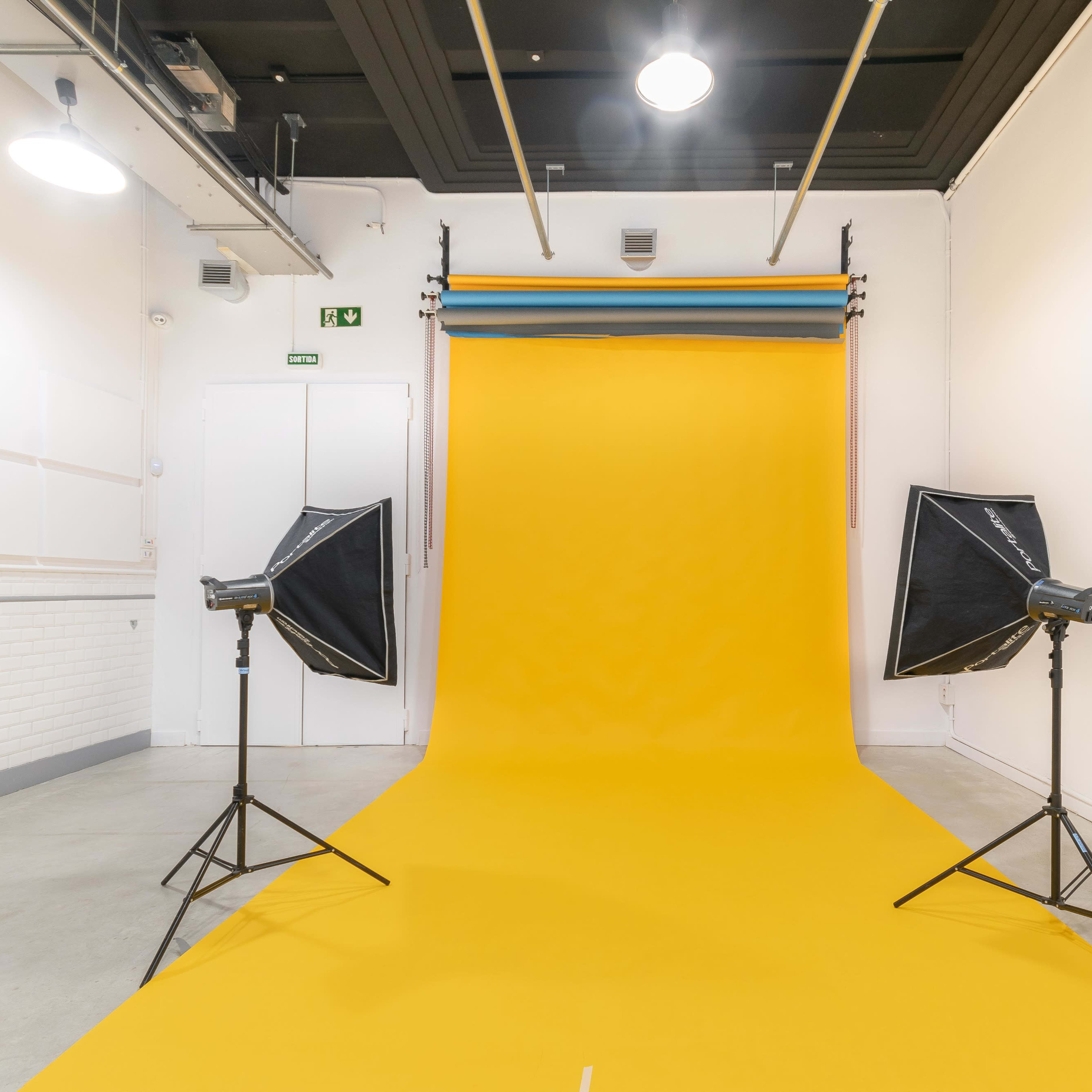 A photography studio with a vibrant yellow backdrop and two softbox lights positioned on either side.