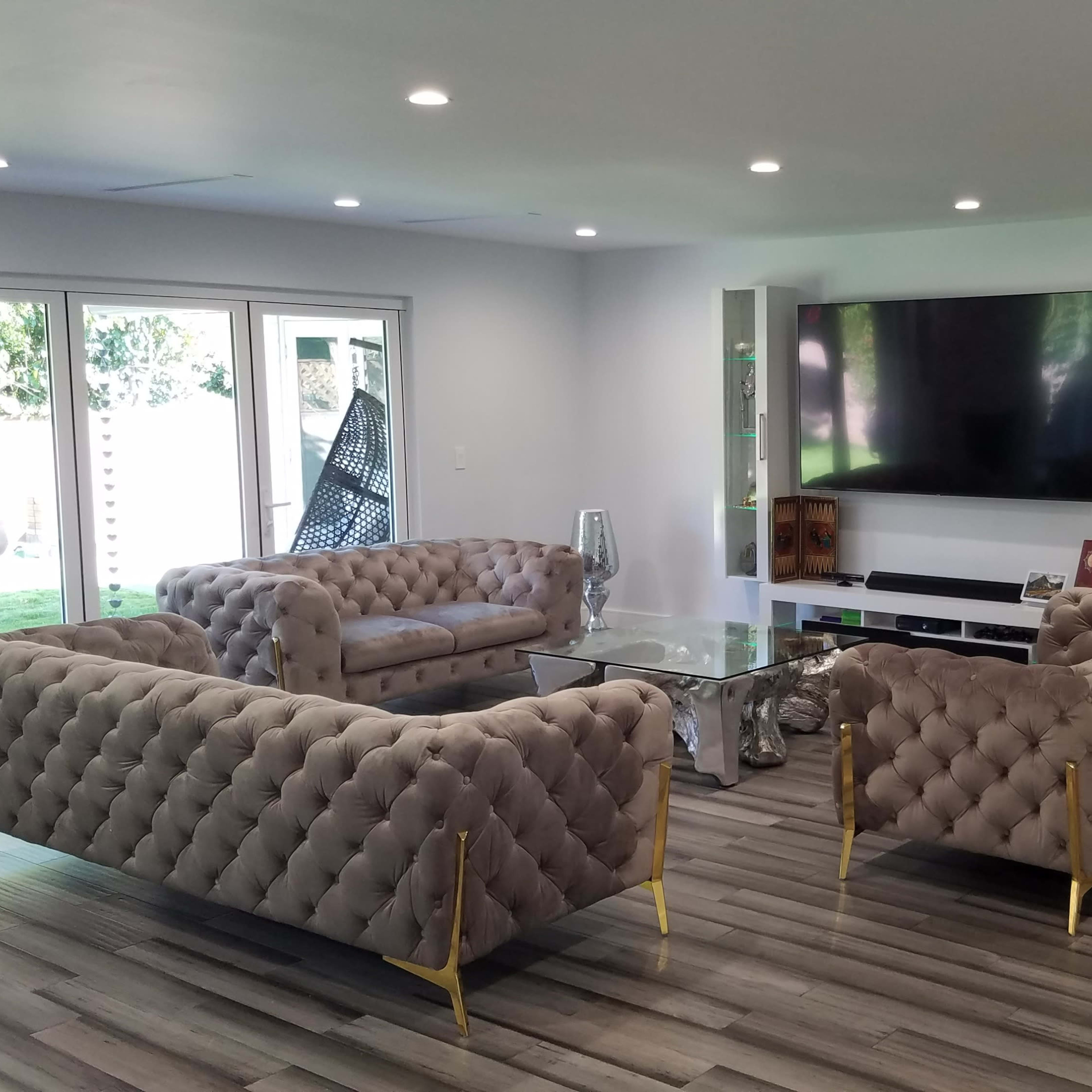 A modern living room with two tufted sofas facing each other, a glass coffee table in the center, and a large television mounted on the wall above a media console.