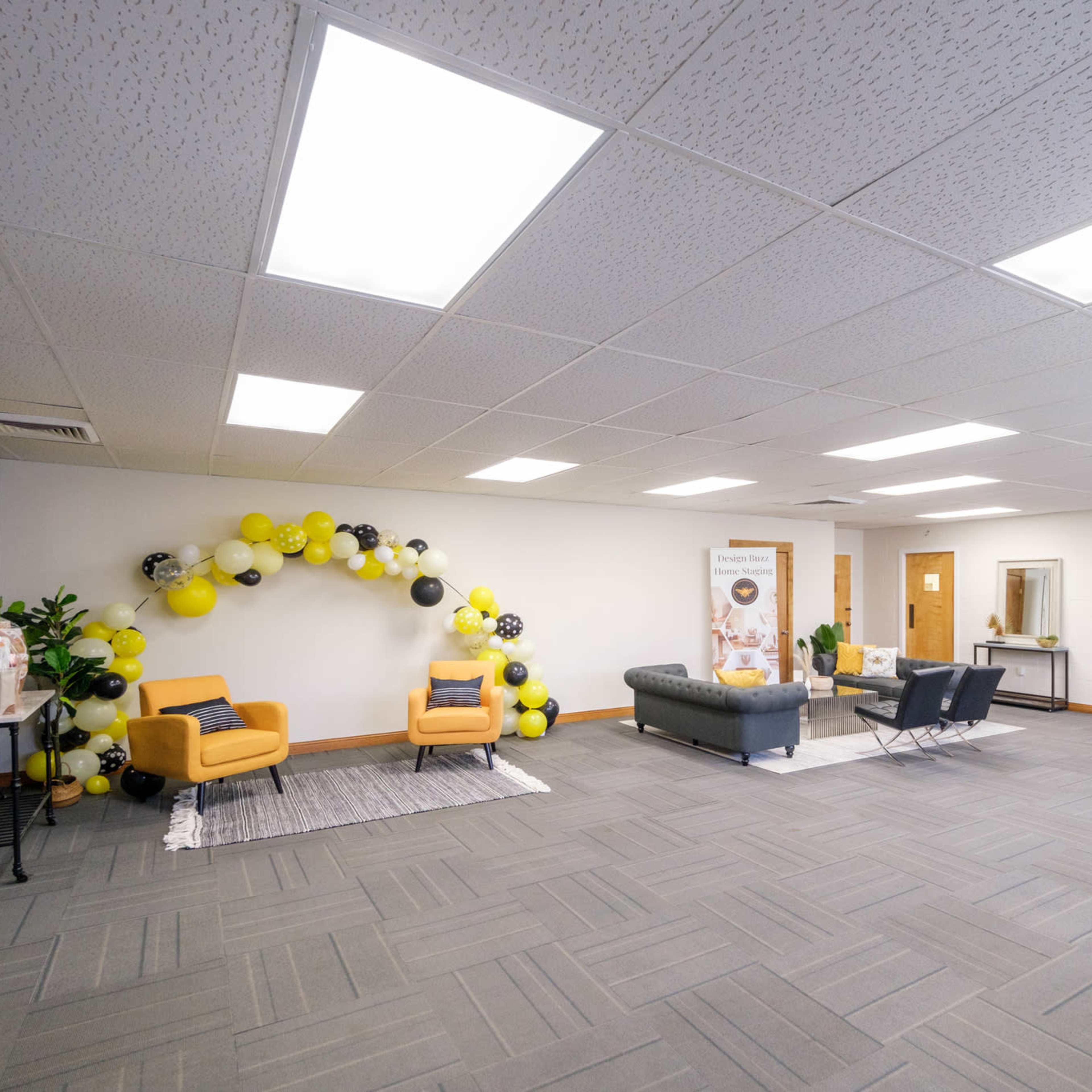 A spacious room featuring two seating areas, decorated with a balloon arch made of yellow and black balloons on one side.