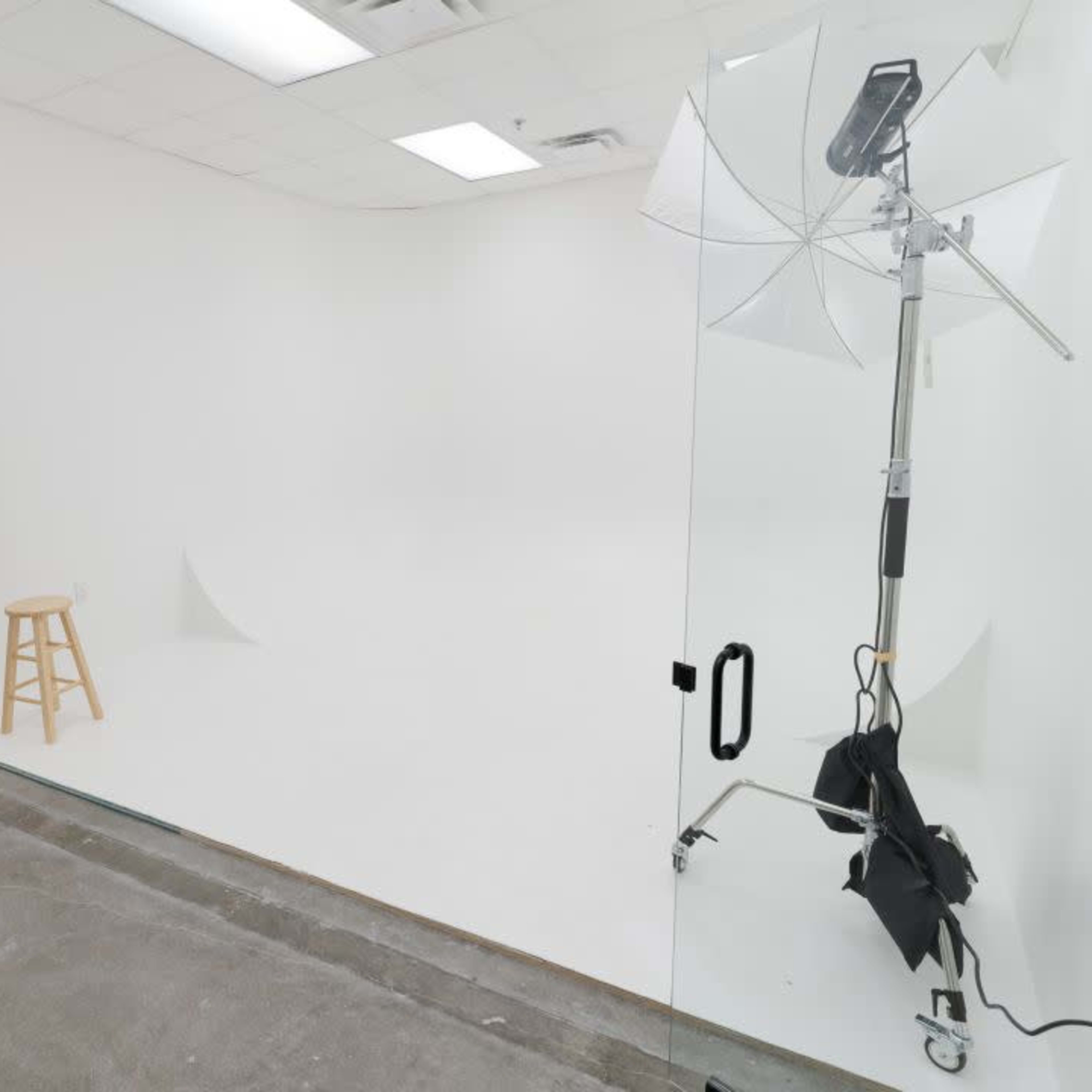 A stark white photography studio featuring lighting equipment and a wooden stool on a seamless backdrop.
