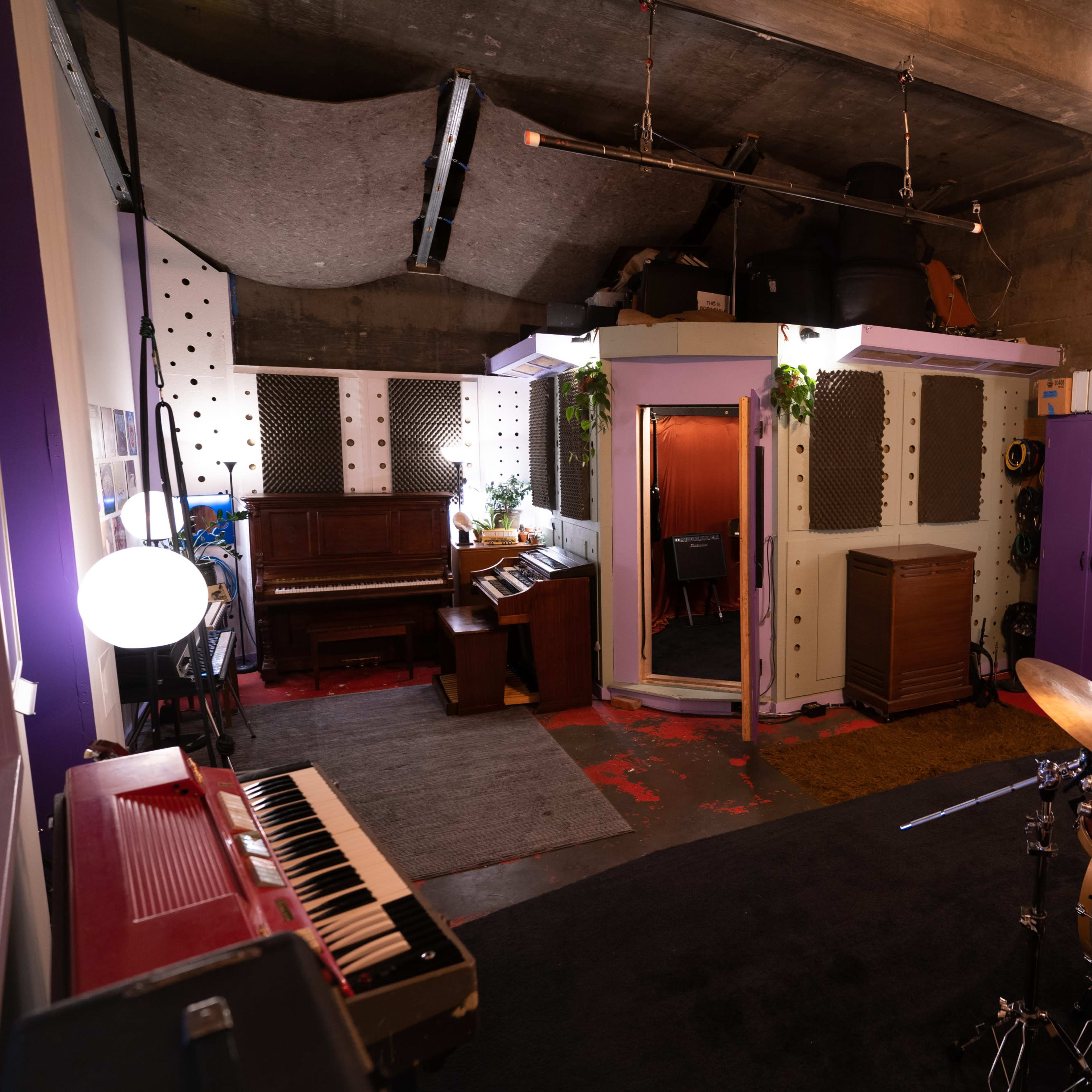 A recording studio with a drum set, a piano, and soundproofing panels on the walls.