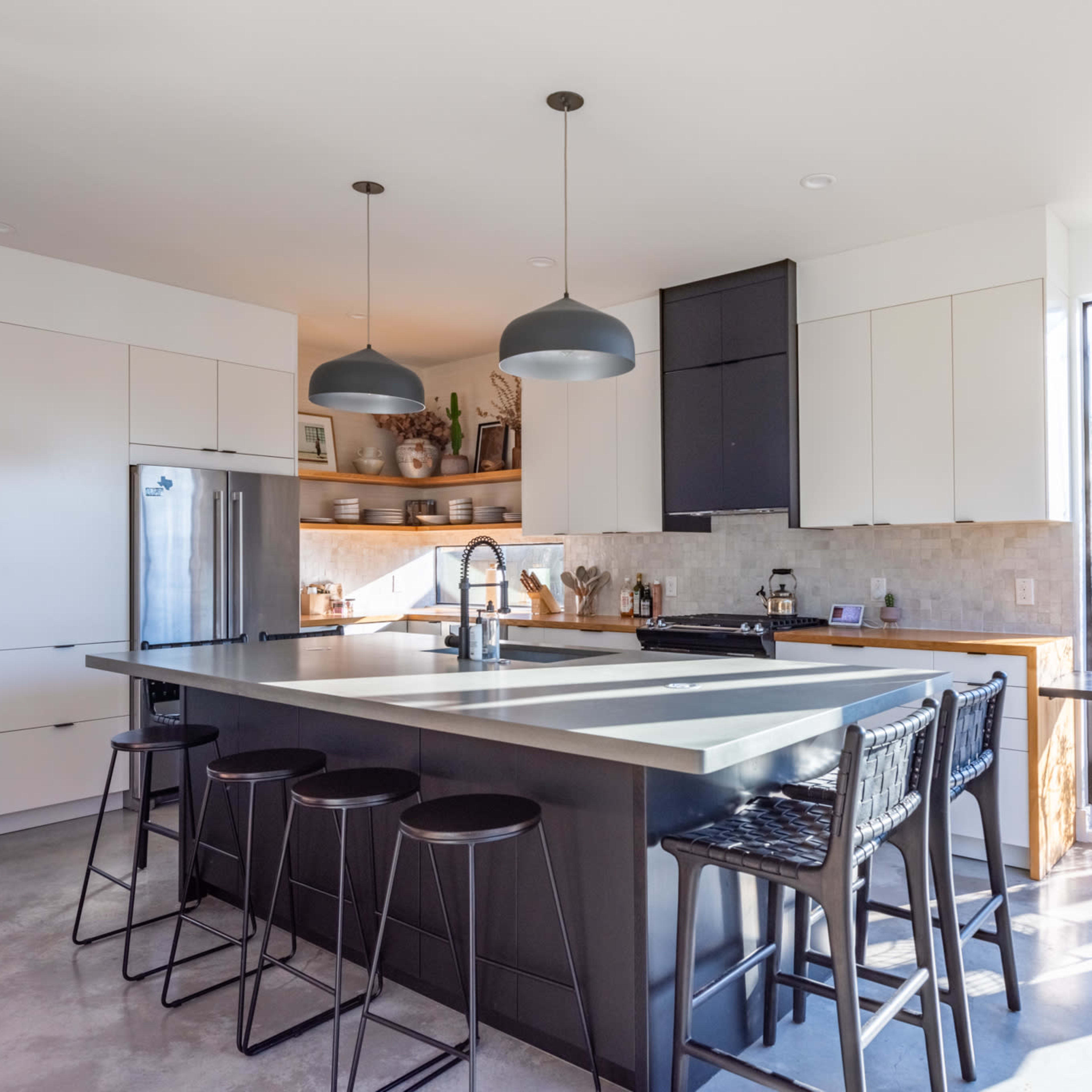 The kitchen features modern cabinetry, a large island with bar seating, and large windows providing natural light.