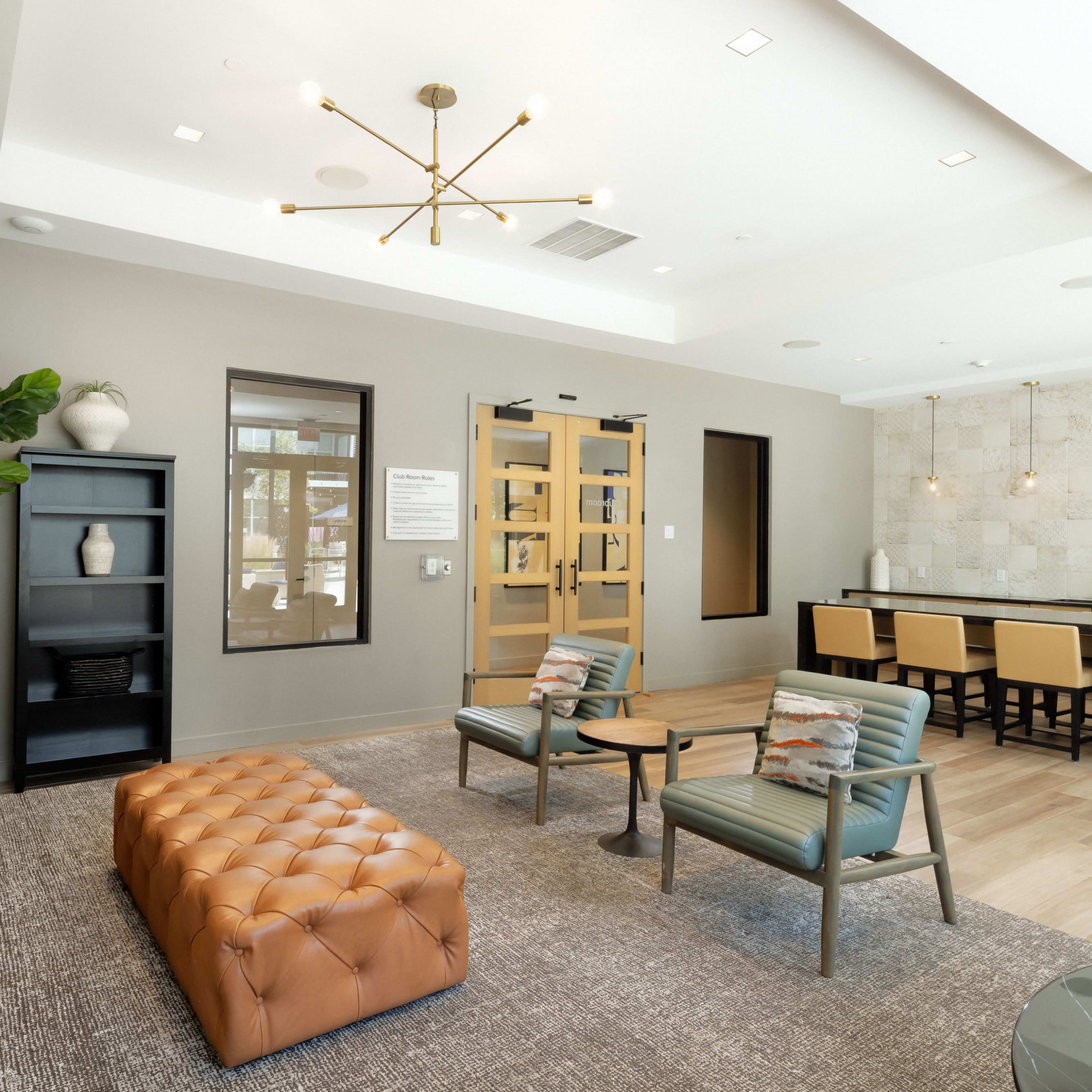 A modern waiting area with a tufted leather ottoman, two chairs, a bookshelf, and a counter with bar stools.