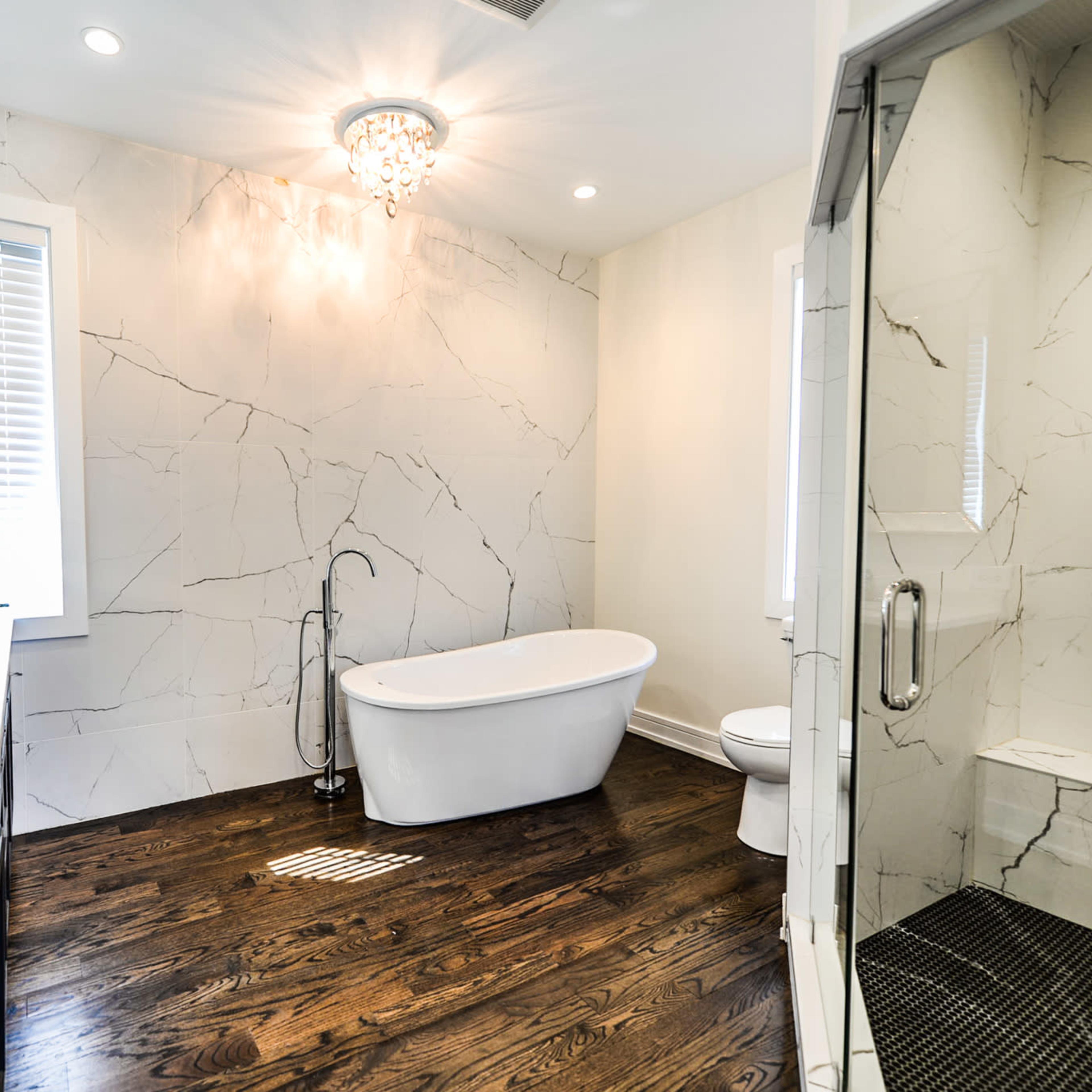 The bathroom features a freestanding tub, dual sinks, a walk-in shower, and marble-patterned walls with hardwood flooring.