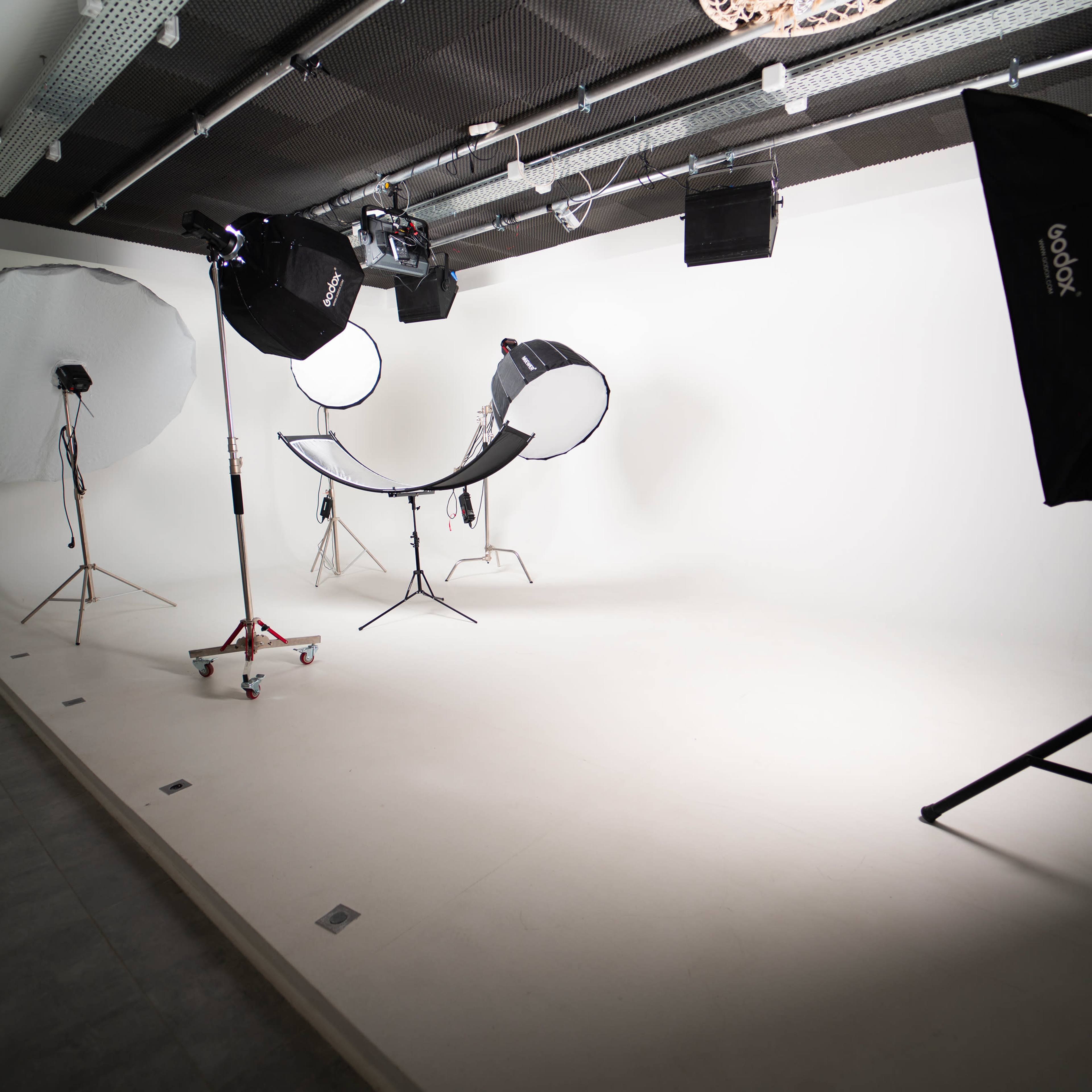 A photography studio with a plain white backdrop, lighting equipment, and a curved chair set up in the center.