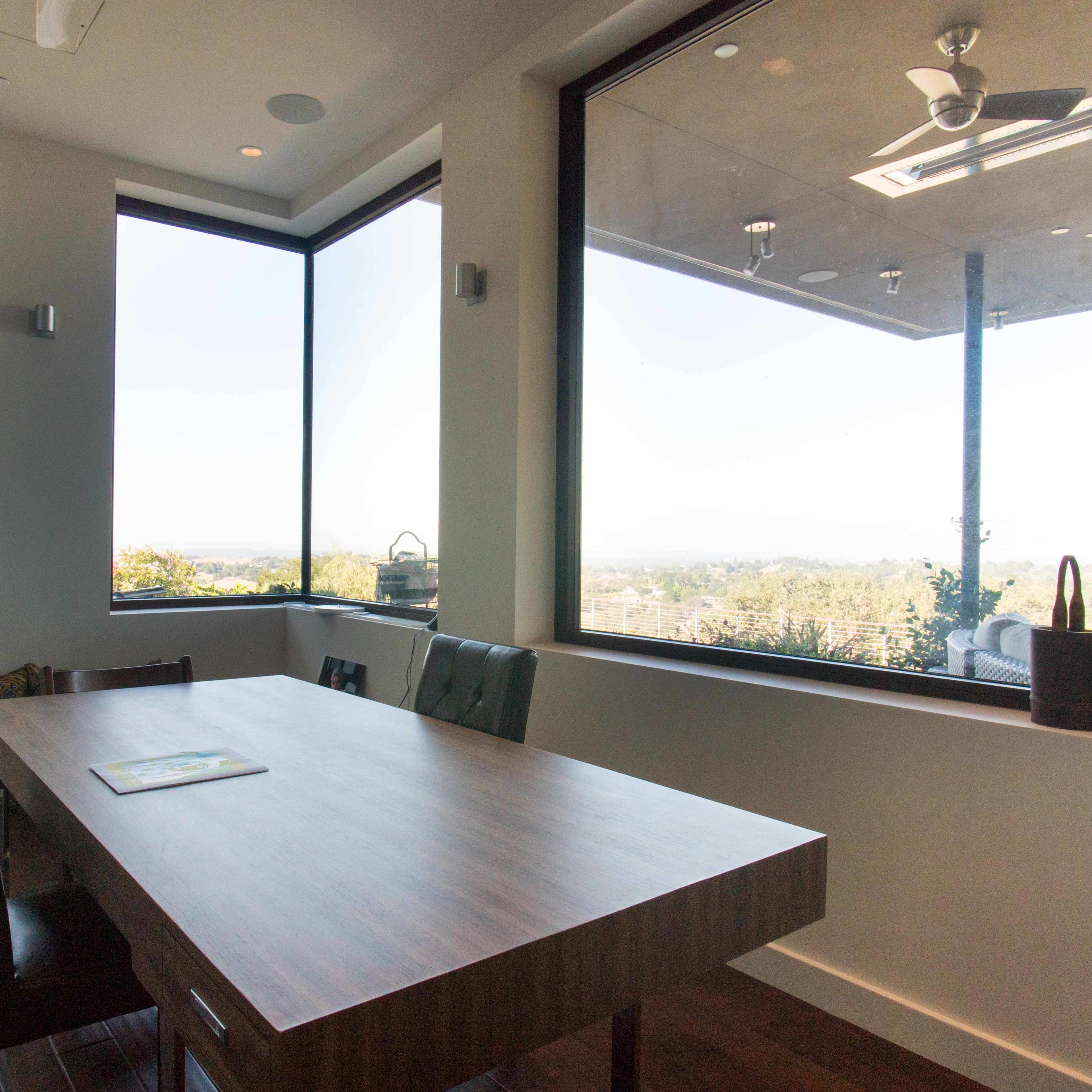 A spacious dining area features a large wooden table and large windows offering a view of the landscape outside.