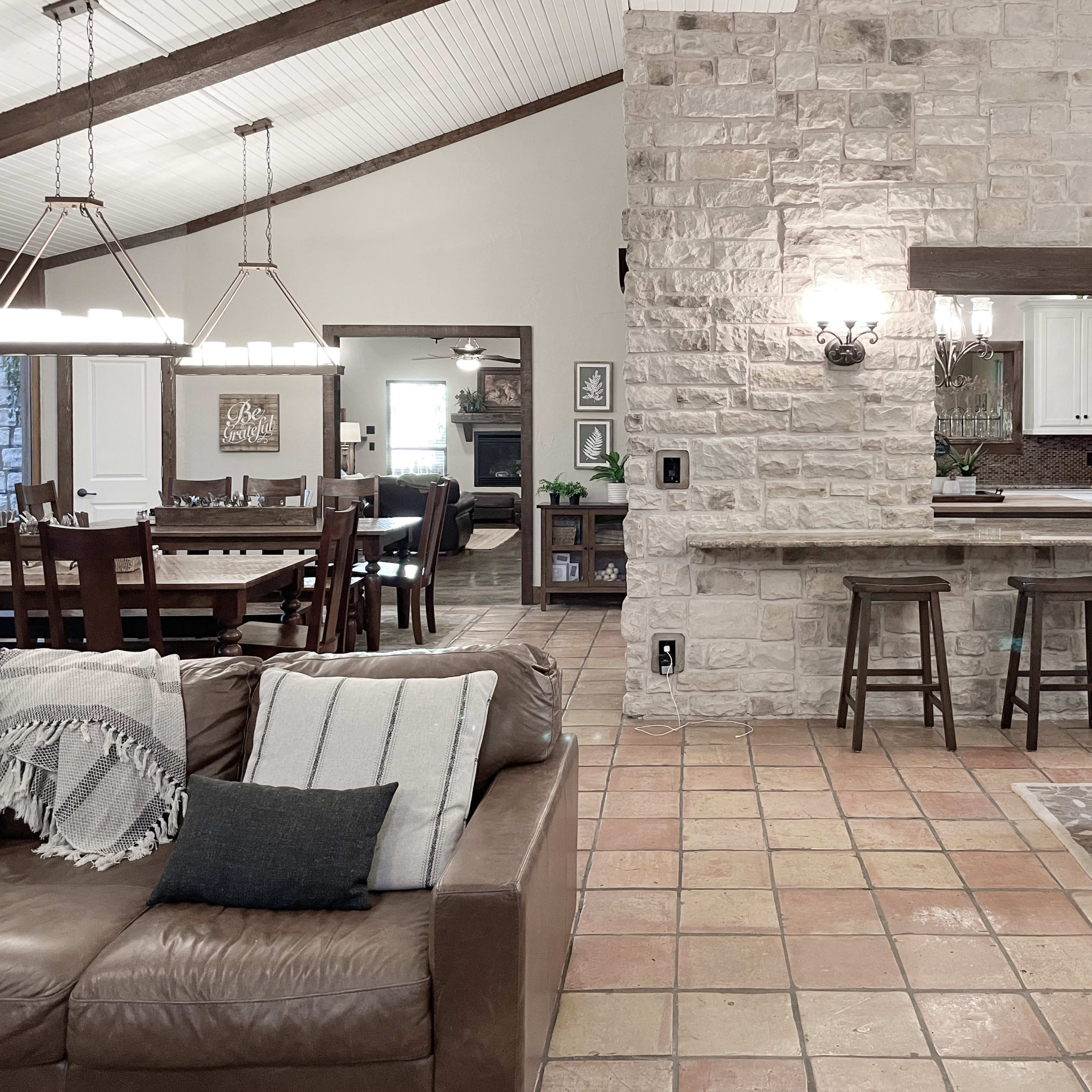 An open-concept living area with a stone wall, a kitchen bar with stools, and a dining area featuring wooden tables and chairs.