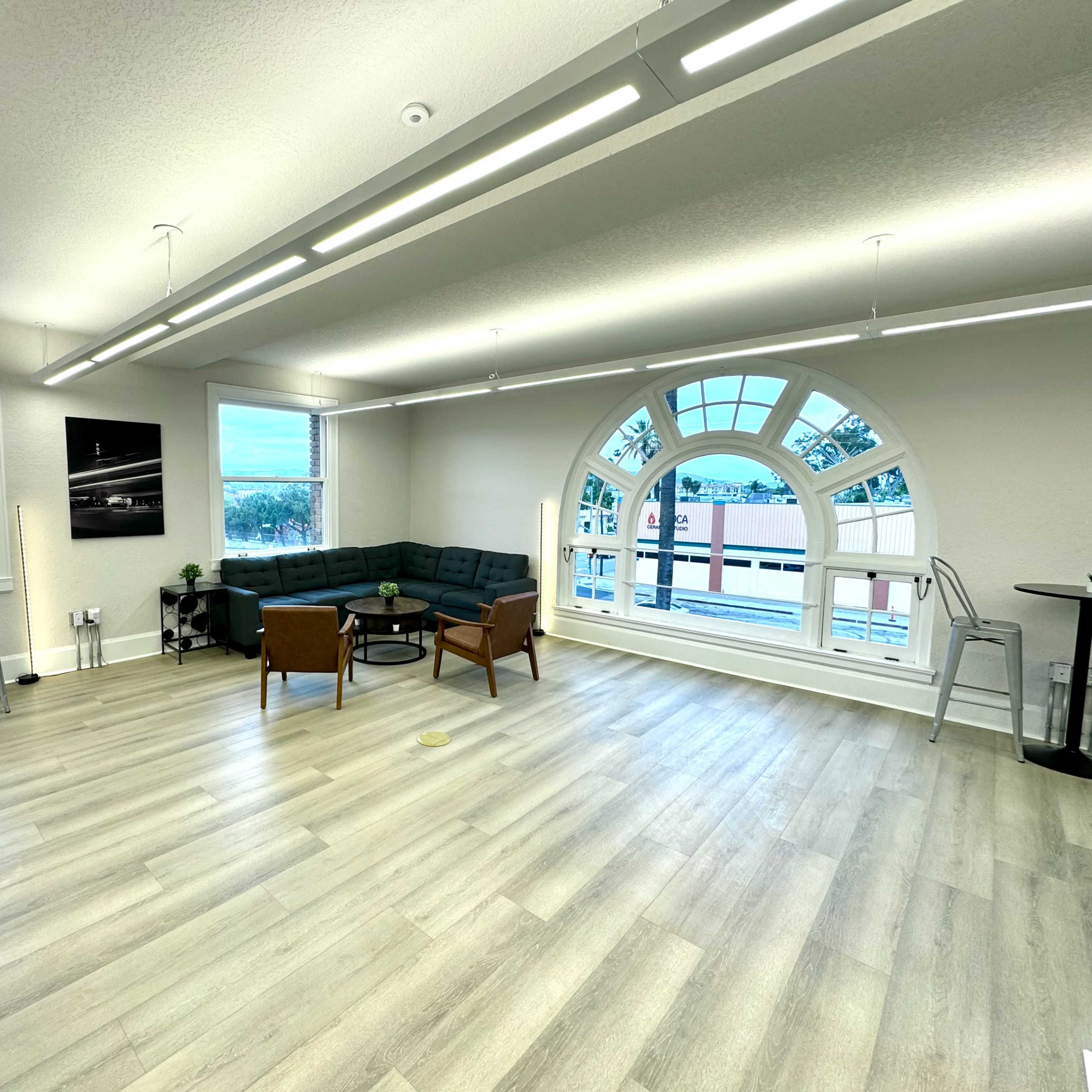 A modern, bright office space with large windows, a sectional couch, and several small tables.