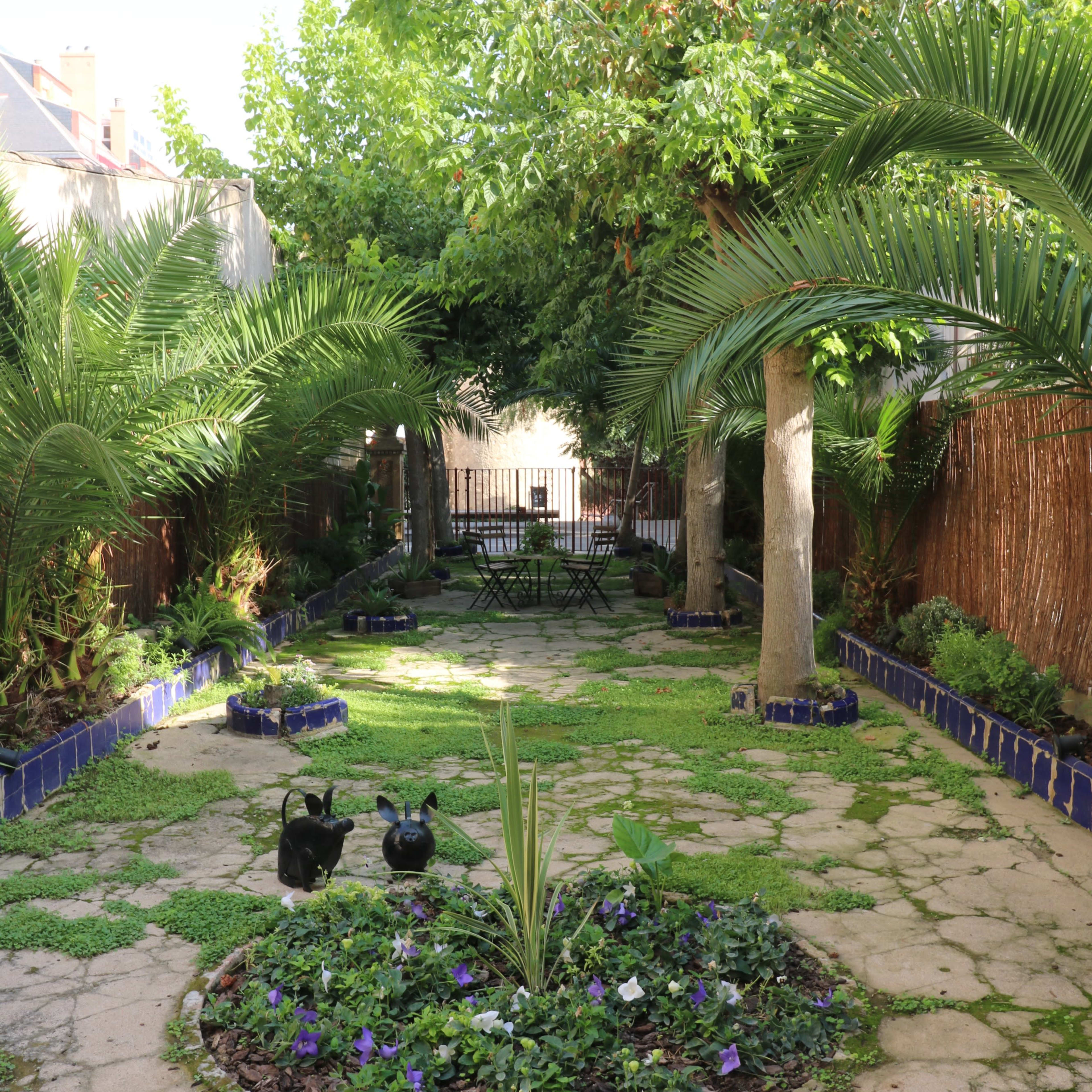 A green garden with palm trees, a circular flowerbed, and a seating area at the back surrounded by lush vegetation.