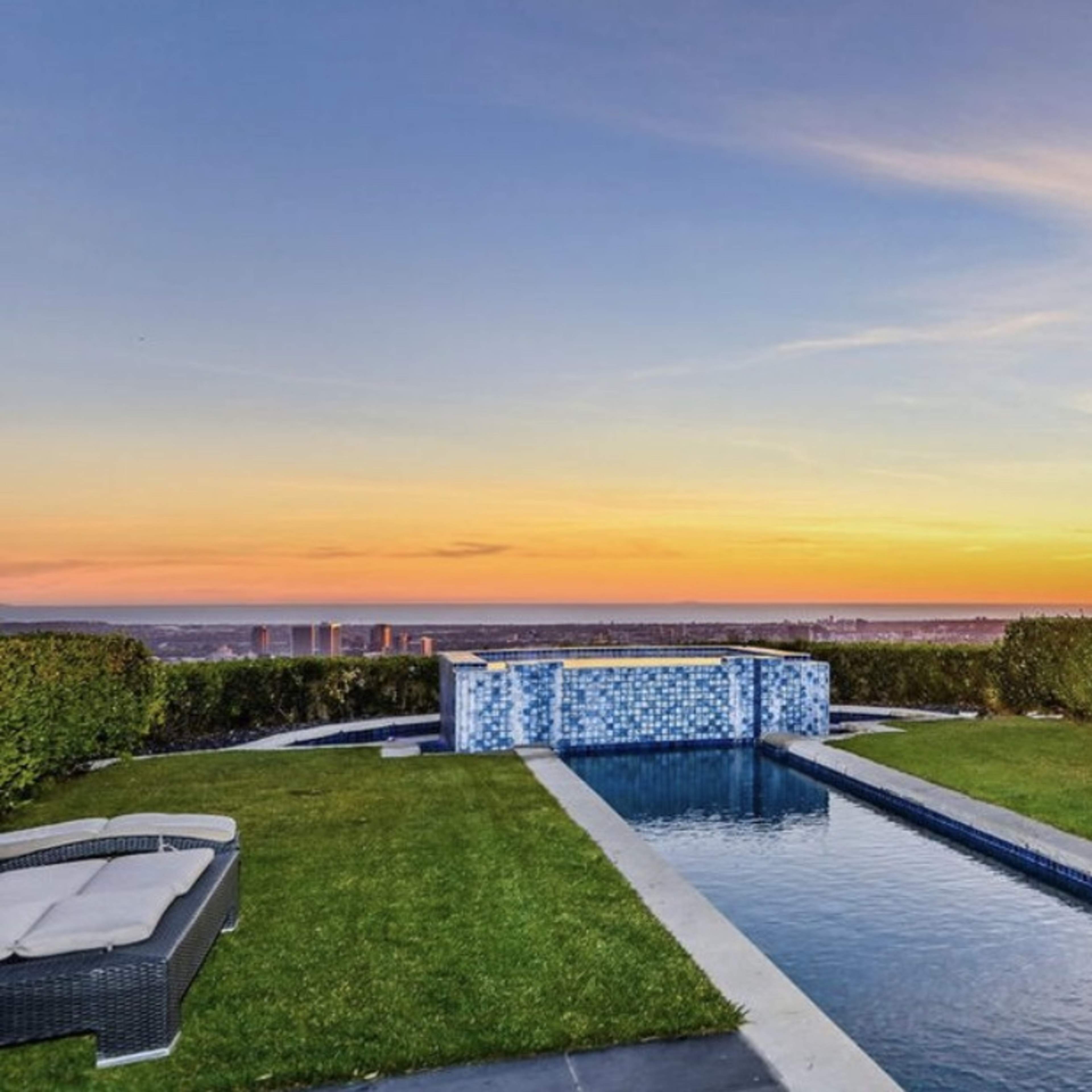 A swimming pool with a sunset backdrop, surrounded by lush greenery and a stone patio.