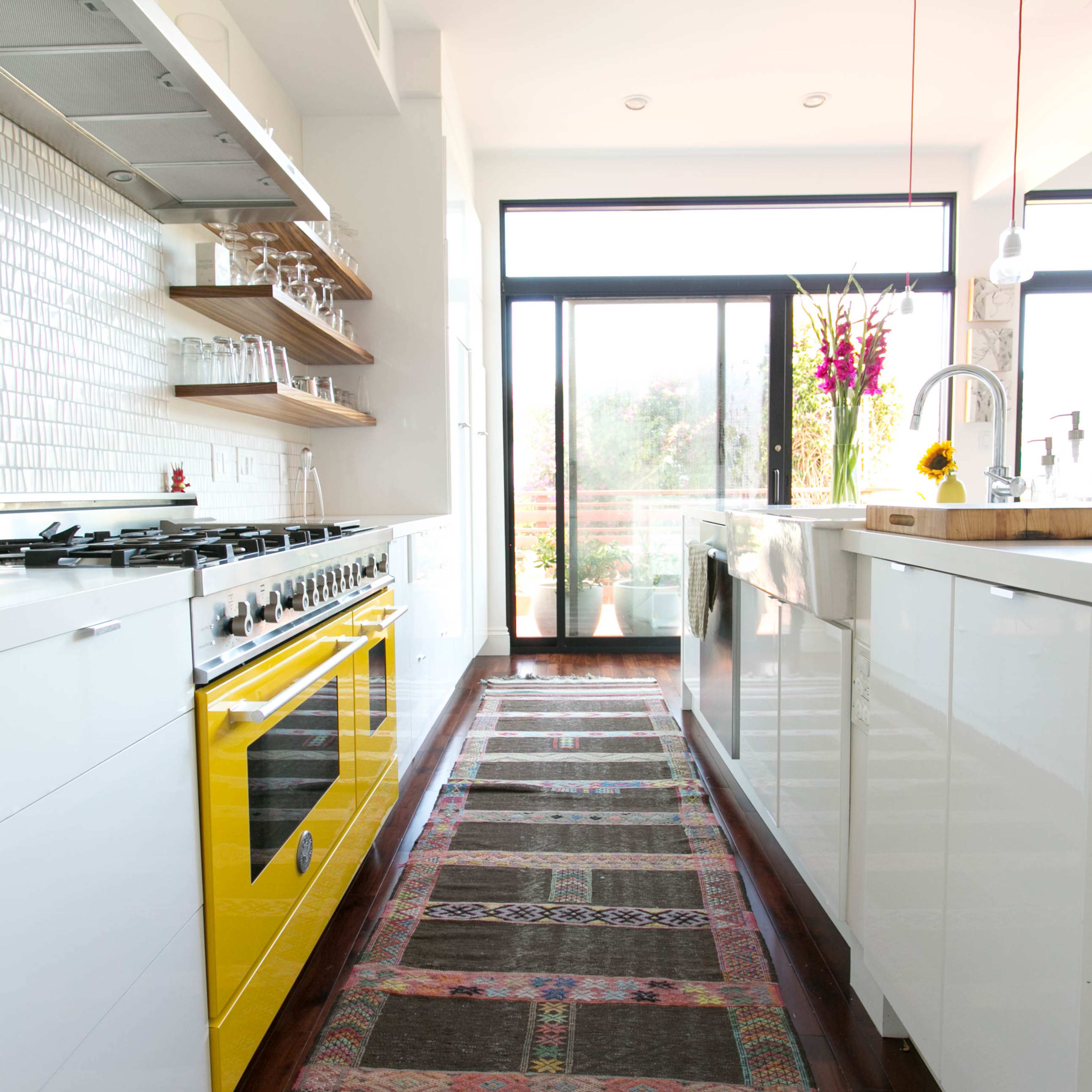 A modern kitchen features white cabinetry, stainless steel appliances, and a yellow stove, with a patterned runner rug extending down the center.
