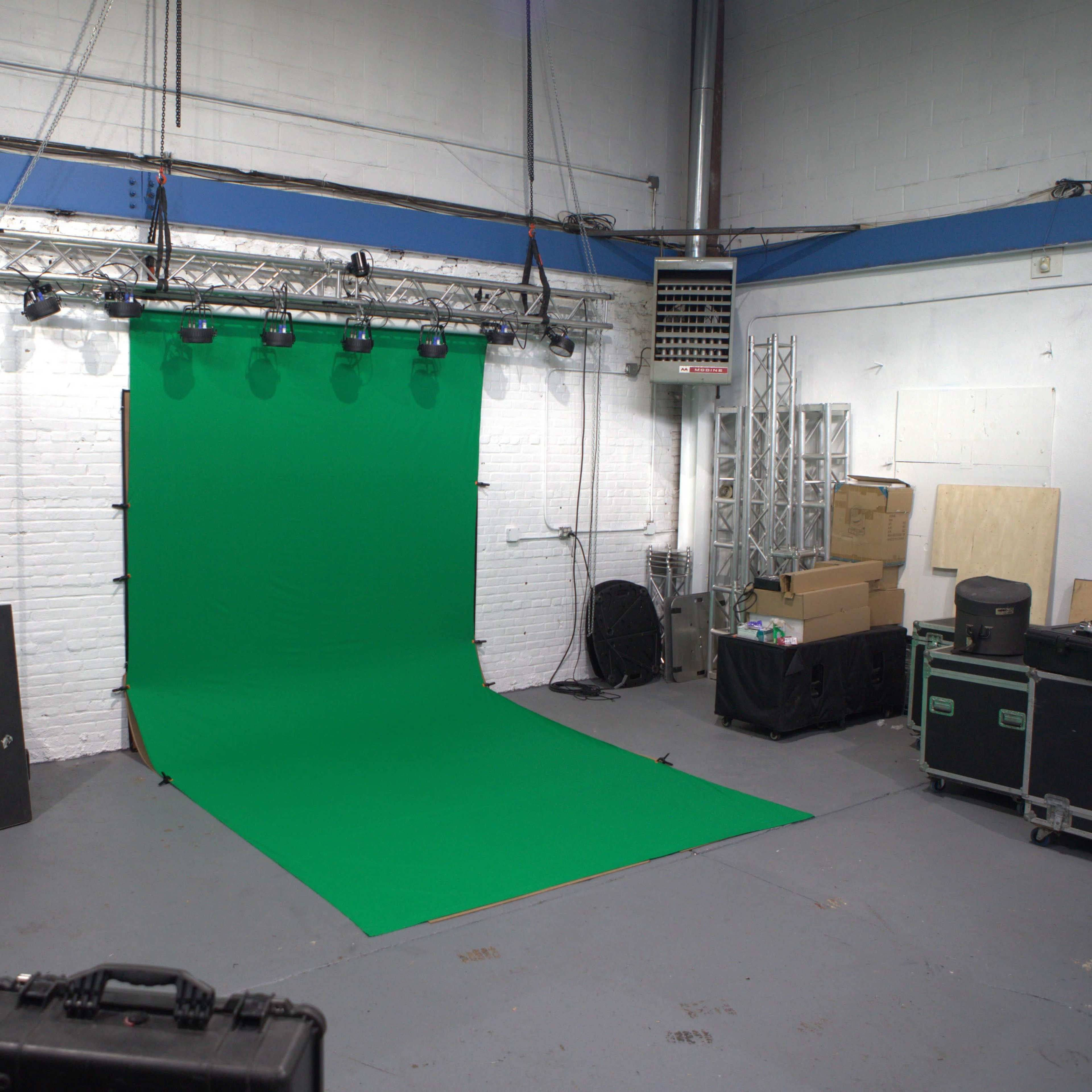 A green screen setup is positioned against a wall in a spacious, cluttered studio.