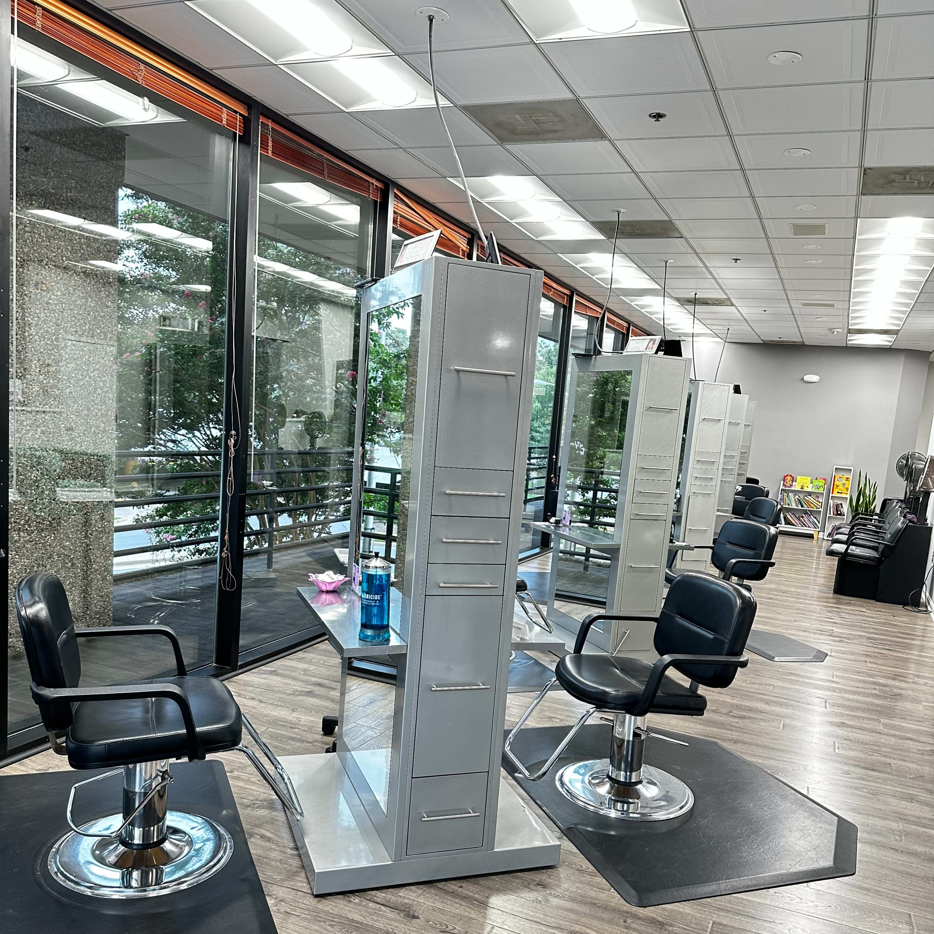 A well-lit hair salon with several styling stations featuring black salon chairs and tall mirrors.