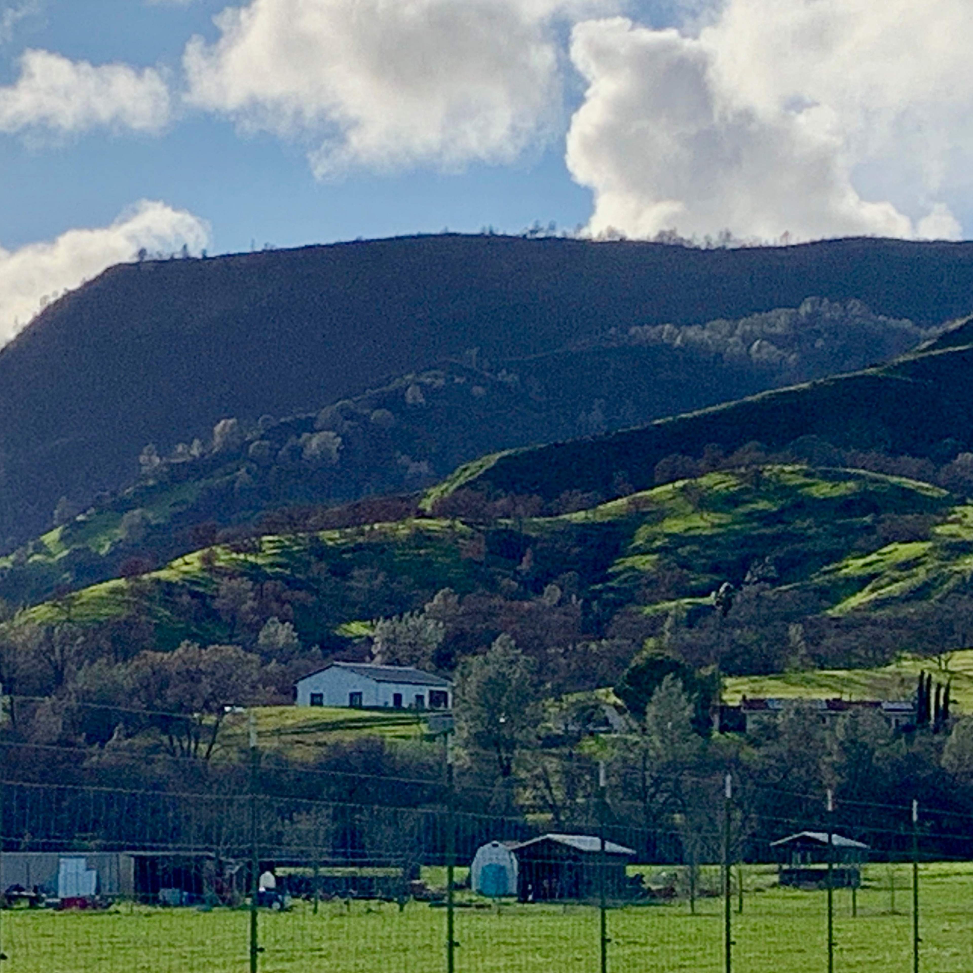 Green hills and mountains in the background with a farmhouse and several outbuildings in a rural landscape.