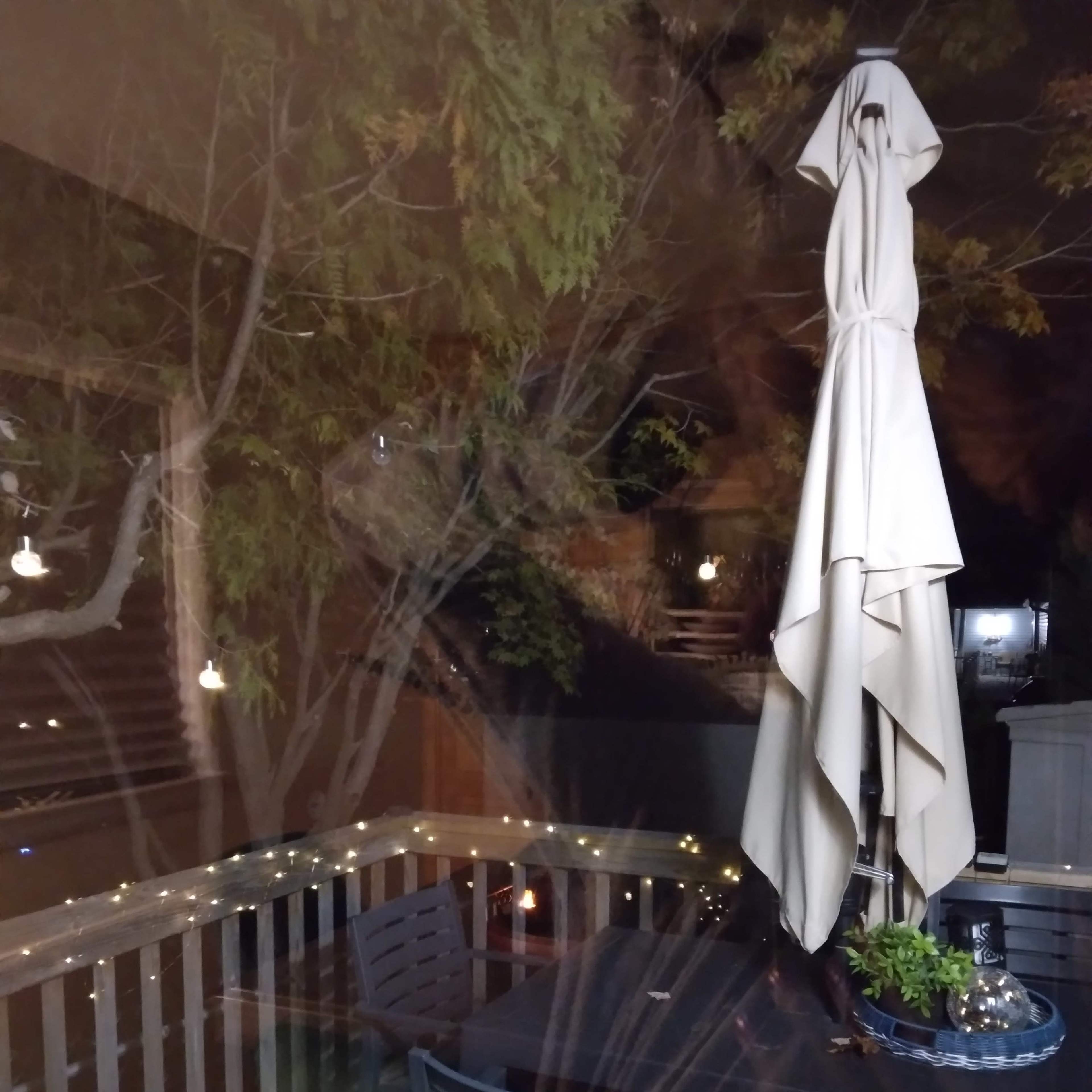 A patio with a table and chairs, featuring an umbrella, surrounded by string lights and trees at night.