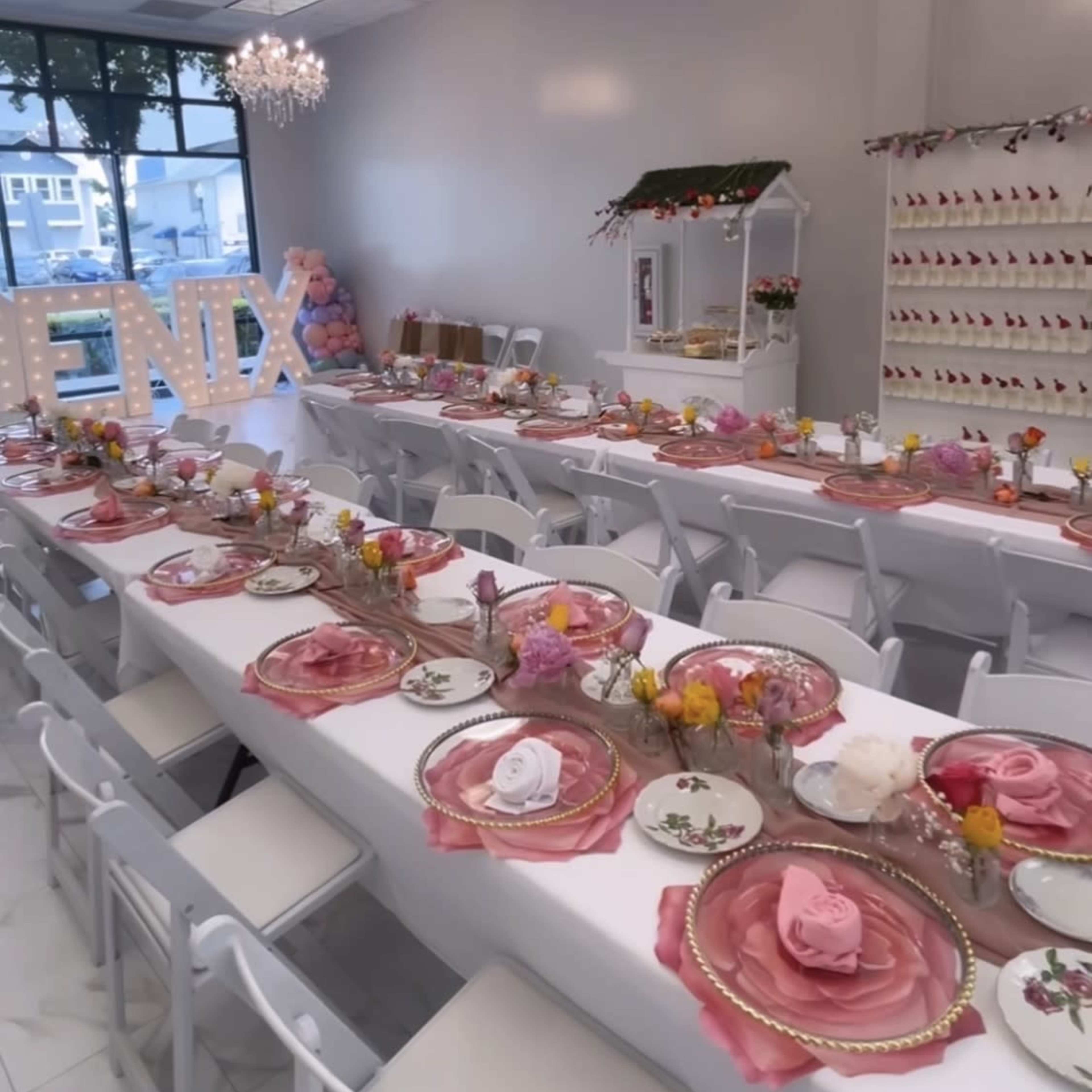 A brightly lit event space features long tables set with floral centerpieces and elegant place settings, adorned with decorative napkins.