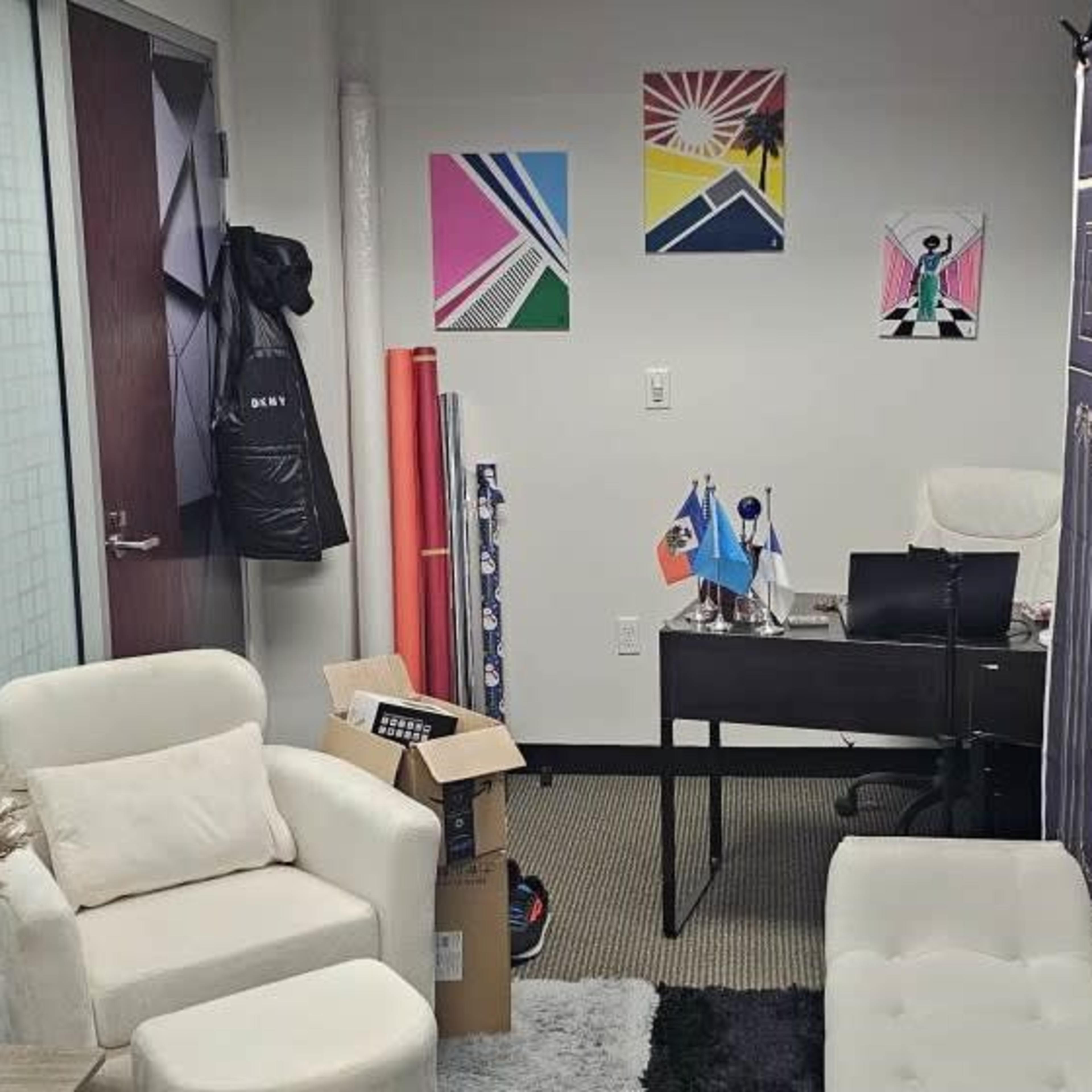 An office space with a desk, two white chairs, colorful wall art, and a backdrop featuring a door design.