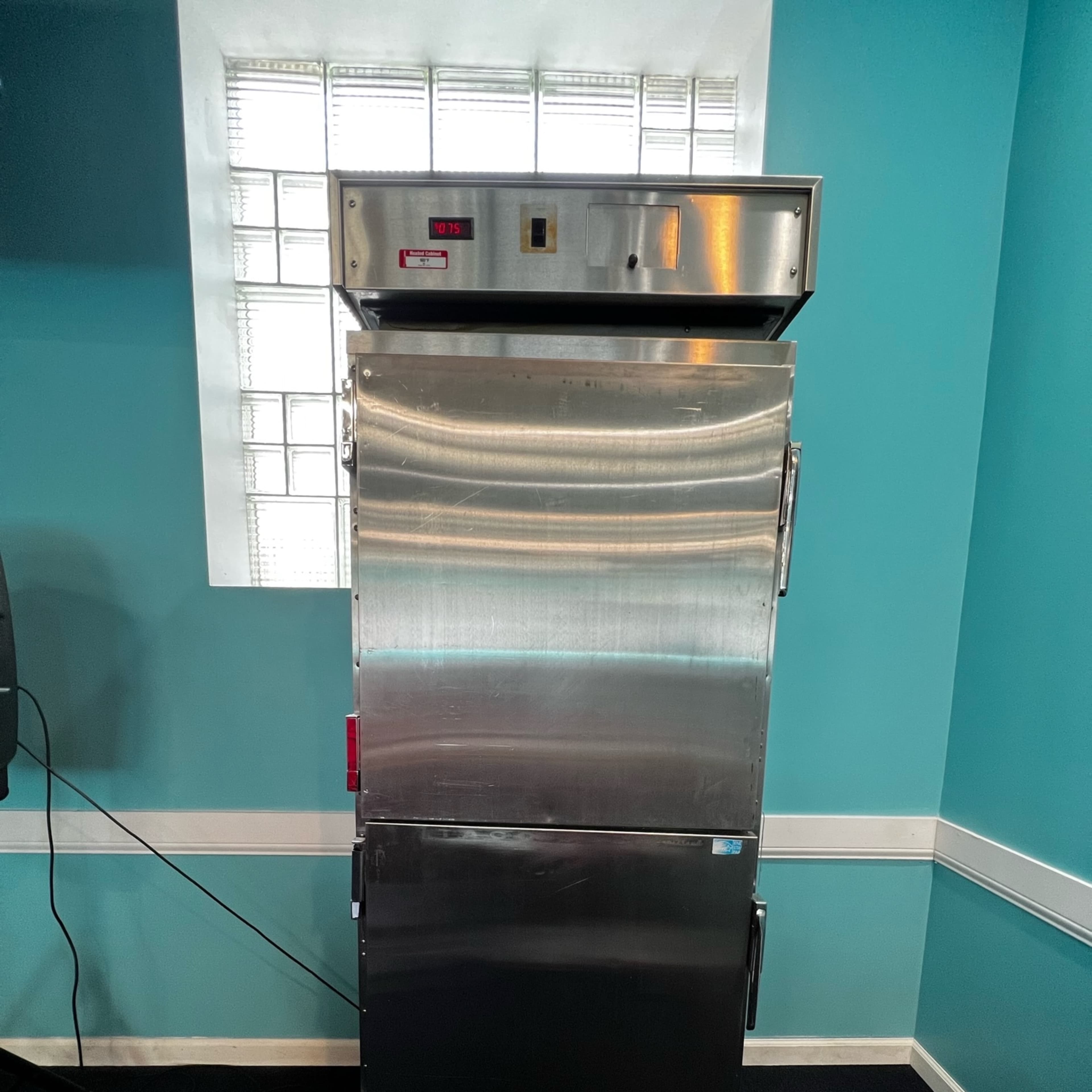 A tall, stainless steel commercial refrigerator situated against a turquoise wall.