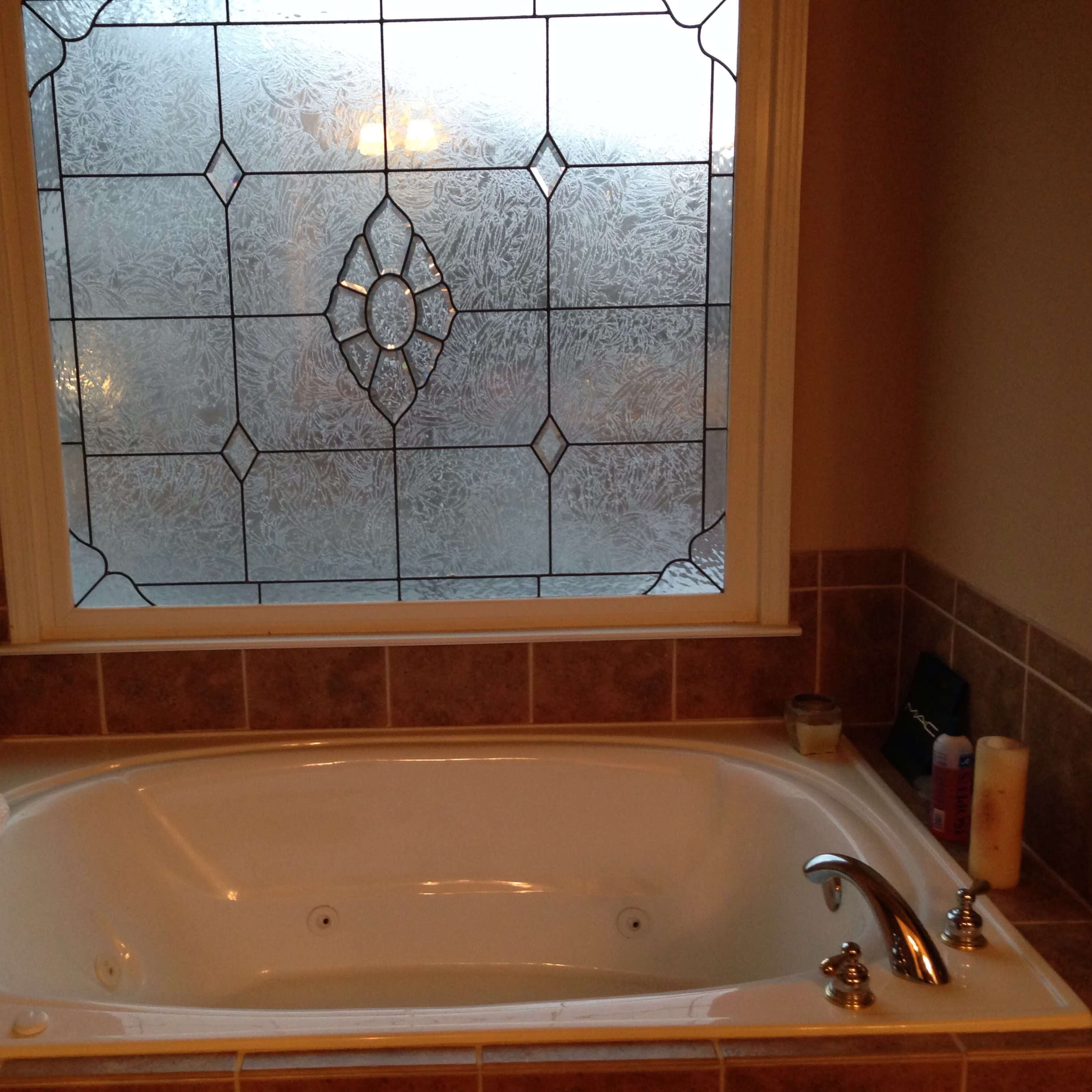 A bathtub is positioned beneath a stained glass window with a floral design.
