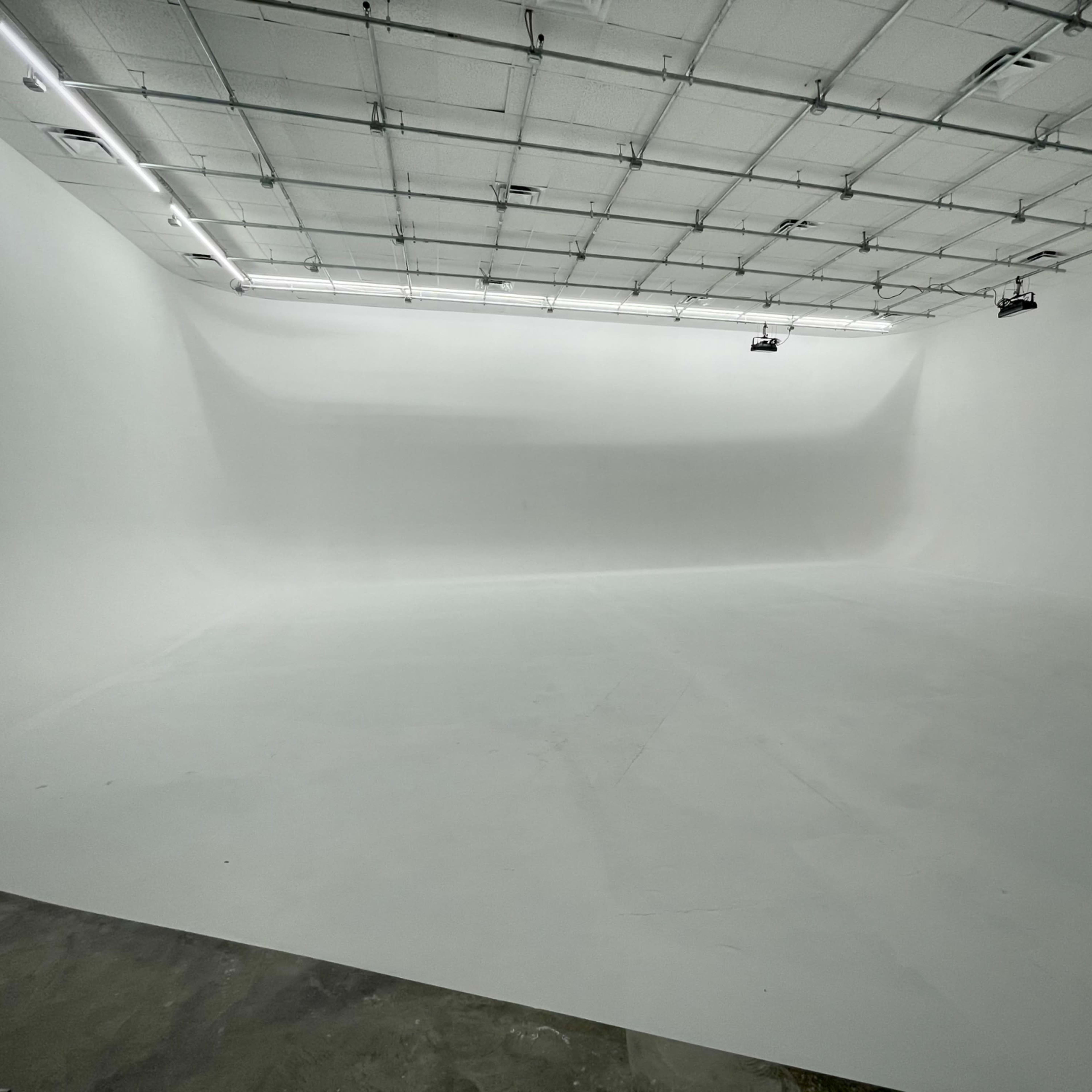 A large, empty studio space with white walls and a smooth floor under bright overhead lighting.