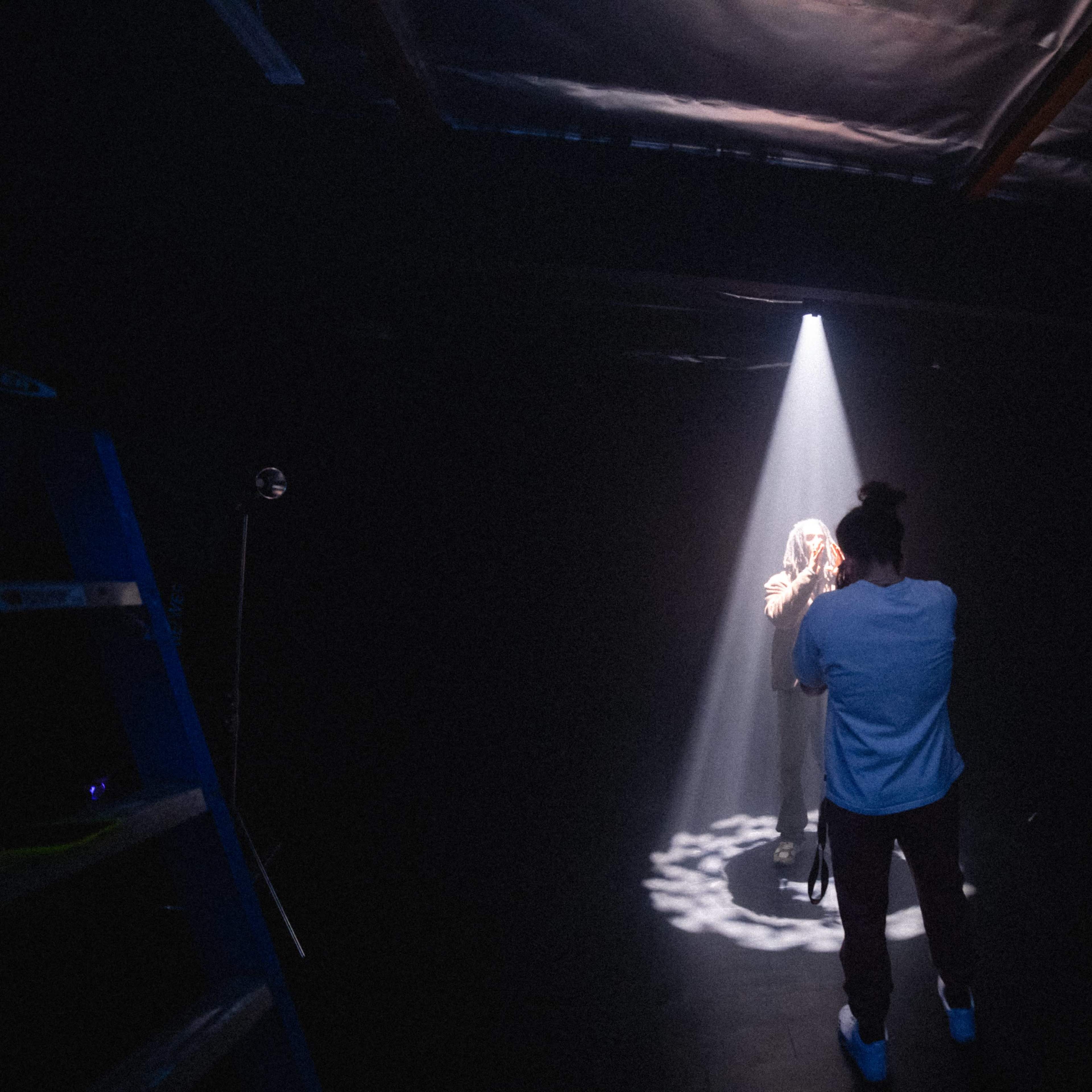 A photographer captures a subject illuminated by a single beam of light in a dark studio.