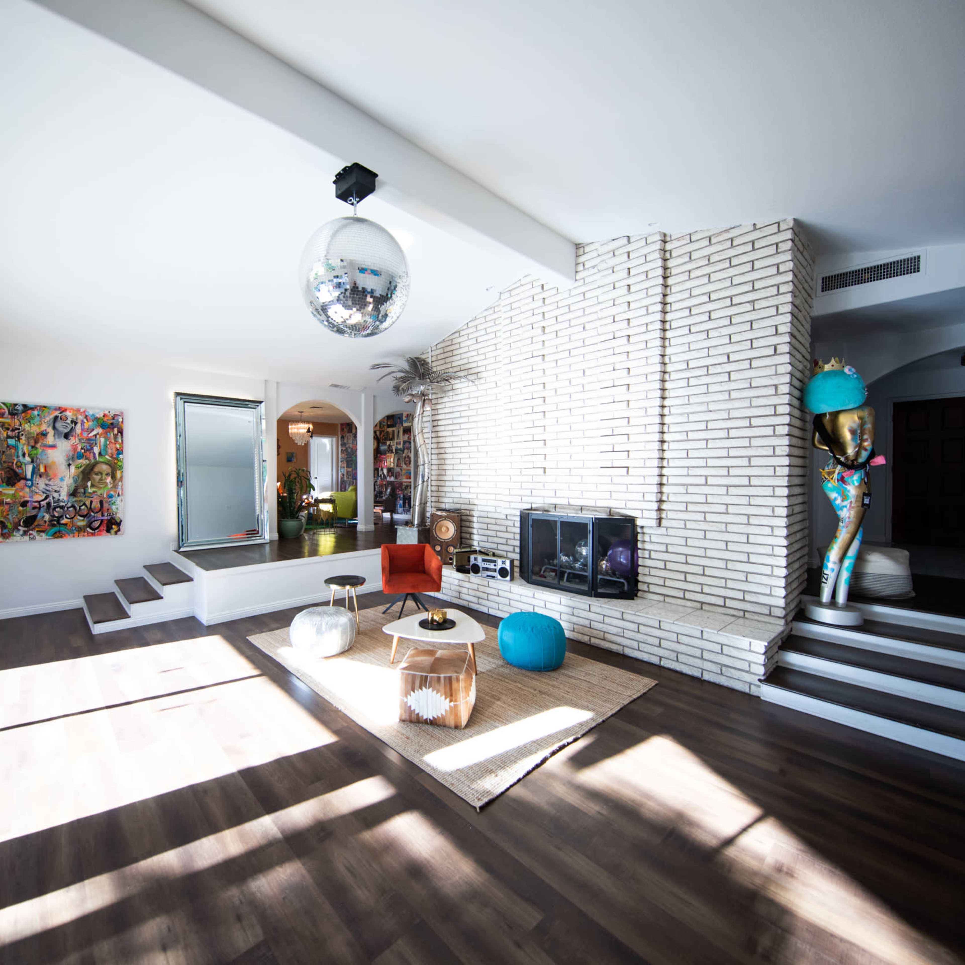 A spacious living room featuring large windows, a disco ball, modern furniture, and a distinctive brick wall.