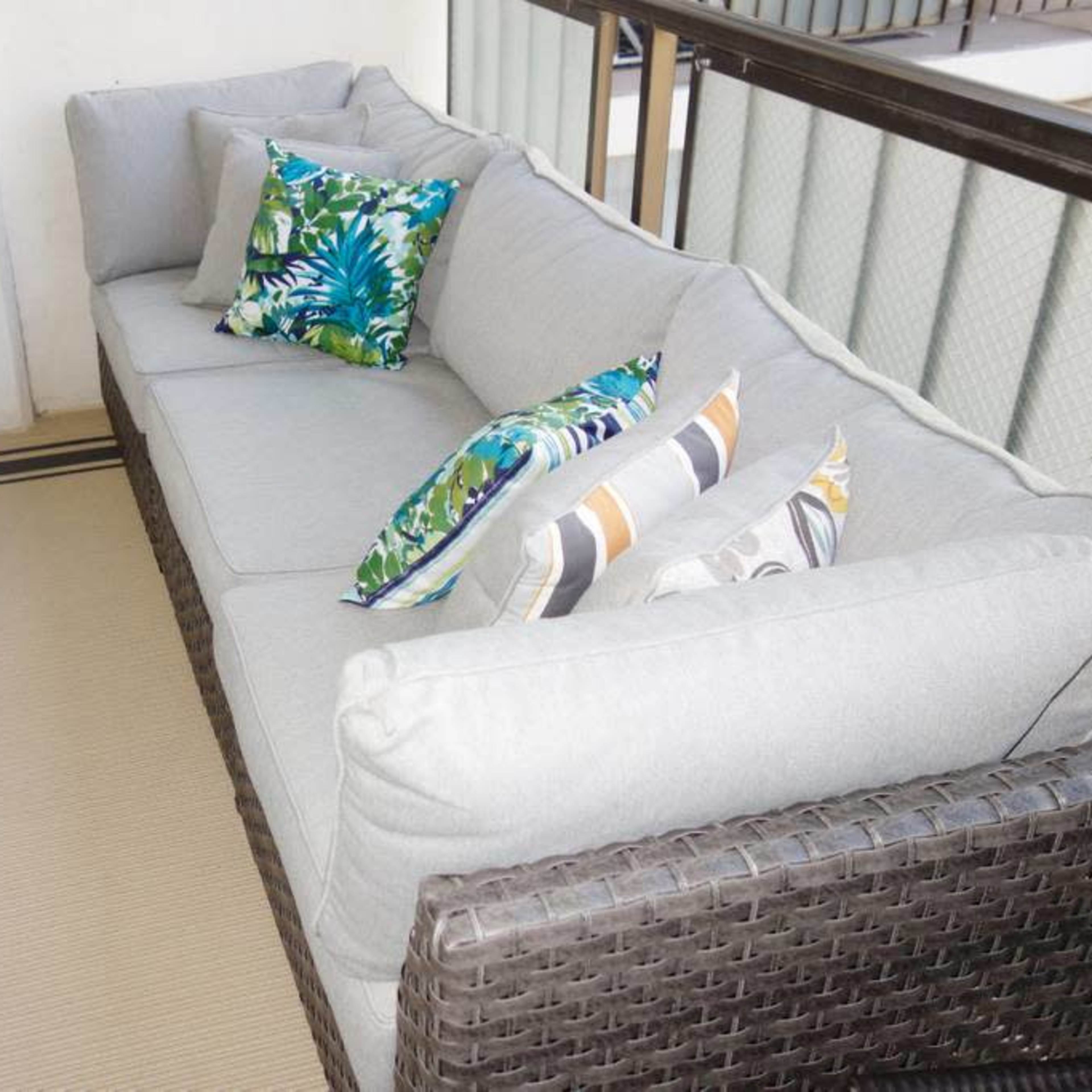 A sectional outdoor sofa with decorative pillows is positioned on a balcony next to a potted plant.