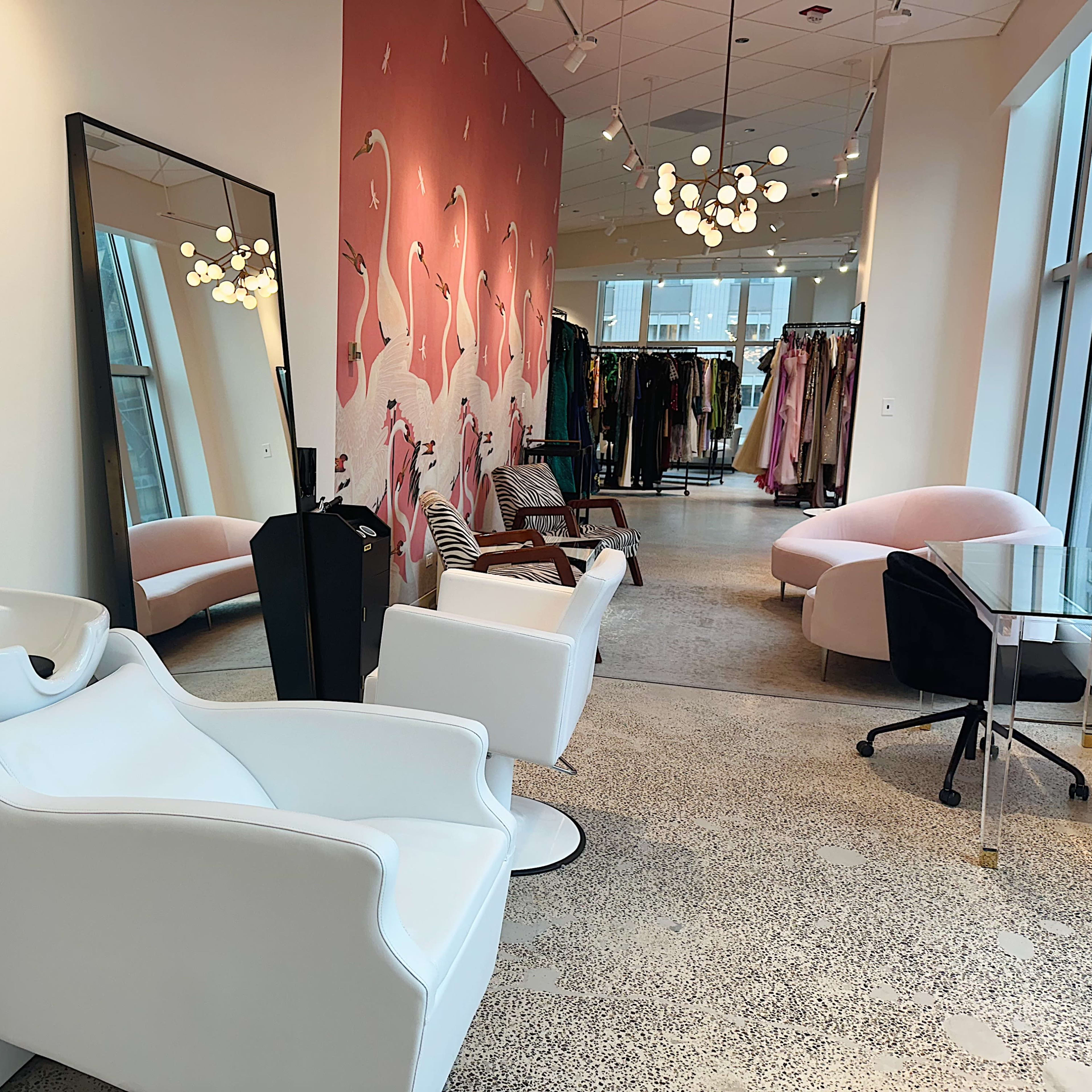 A modern hair salon with white styling chairs, a shampoo station, and a colorful wall mural, alongside a clothing area featuring various garments.