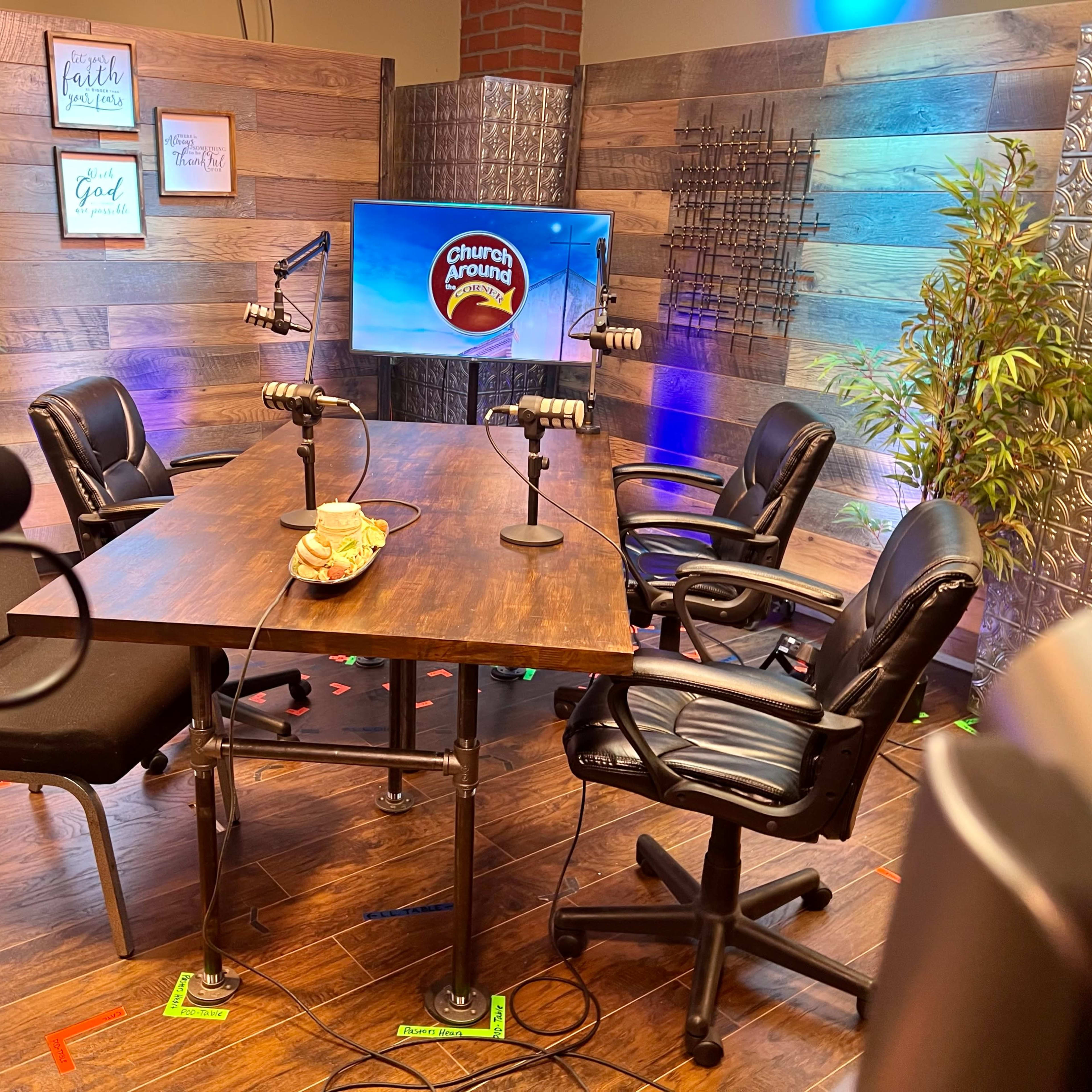 A media setup features a wooden table with four black chairs, microphones, and a screen displaying the "Church Growing" logo against a backdrop of wood paneling and decorative plants.