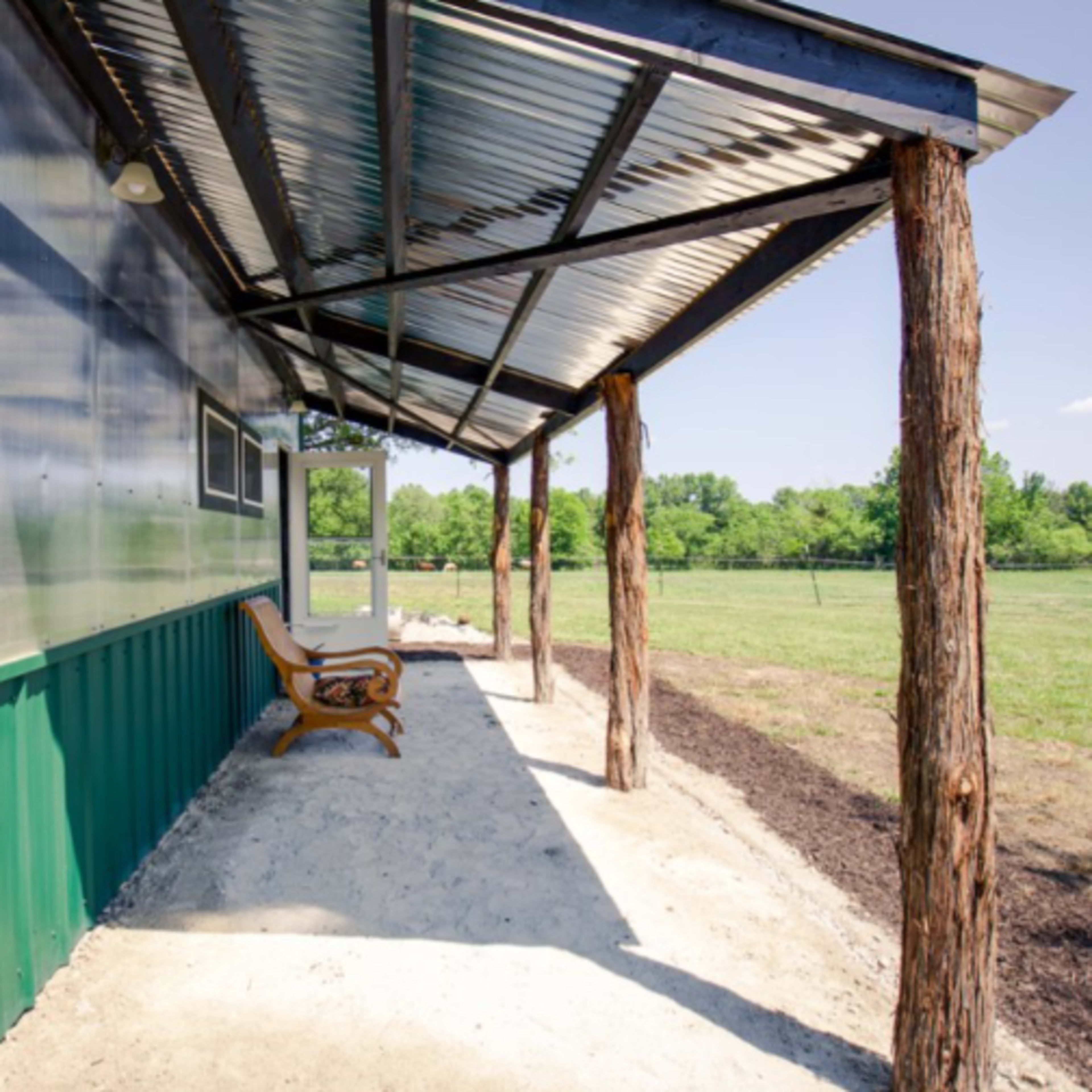 A covered porch with a wooden bench extends alongside a green metal building.
