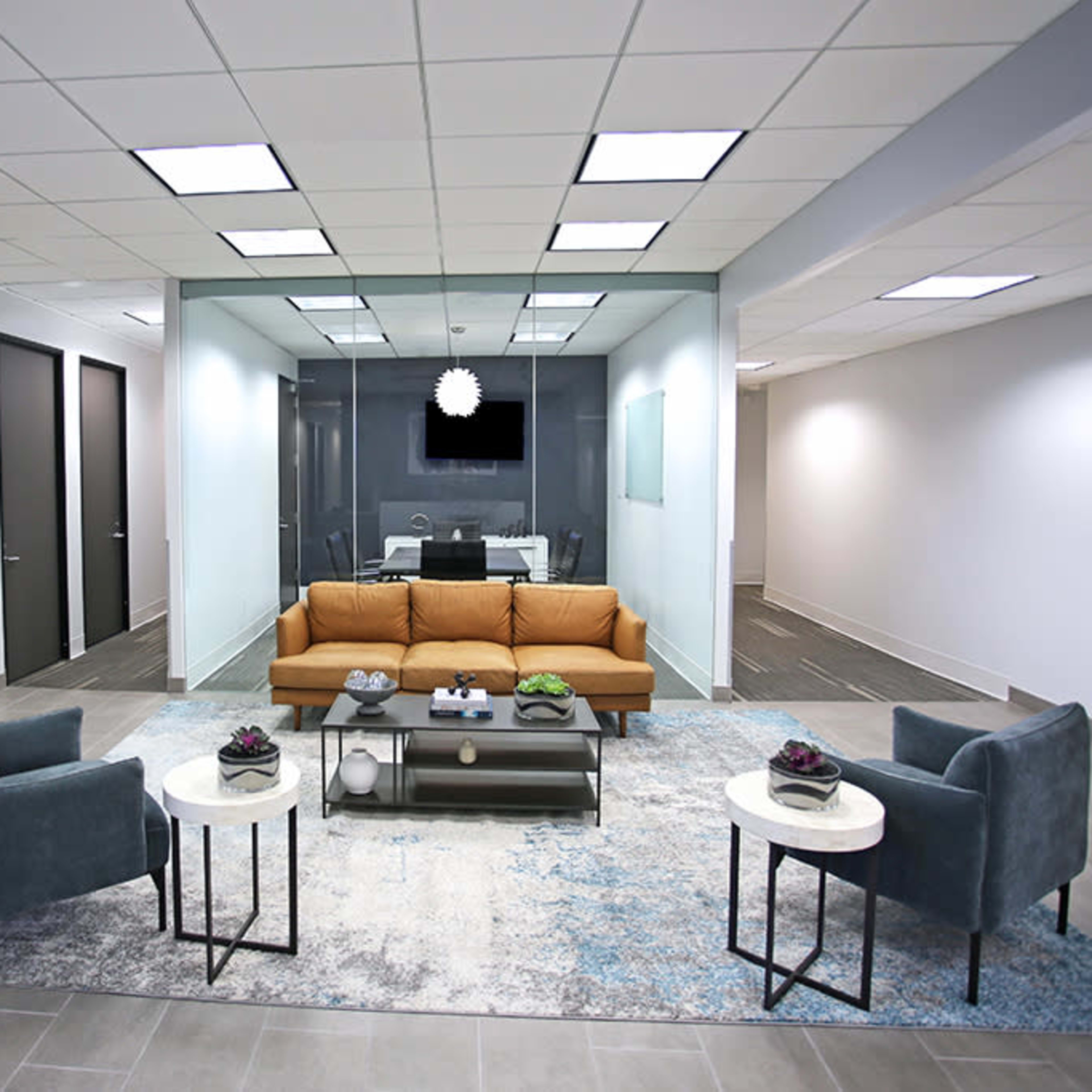 A modern office reception area with a brown sofa, two blue armchairs, and a coffee table centered on a patterned rug.