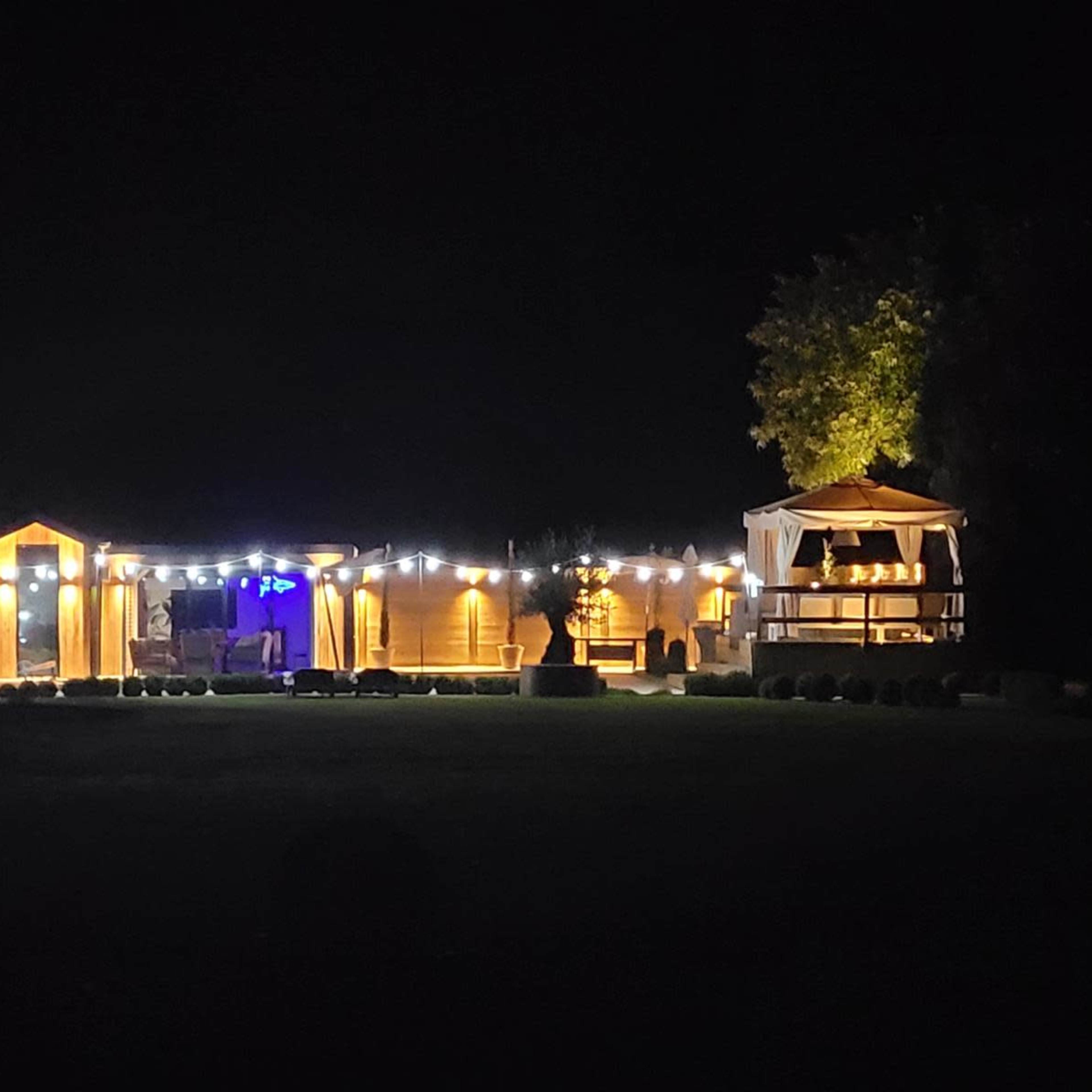 A well-lit outdoor venue features string lights illuminating tents and a gazebo at night.
