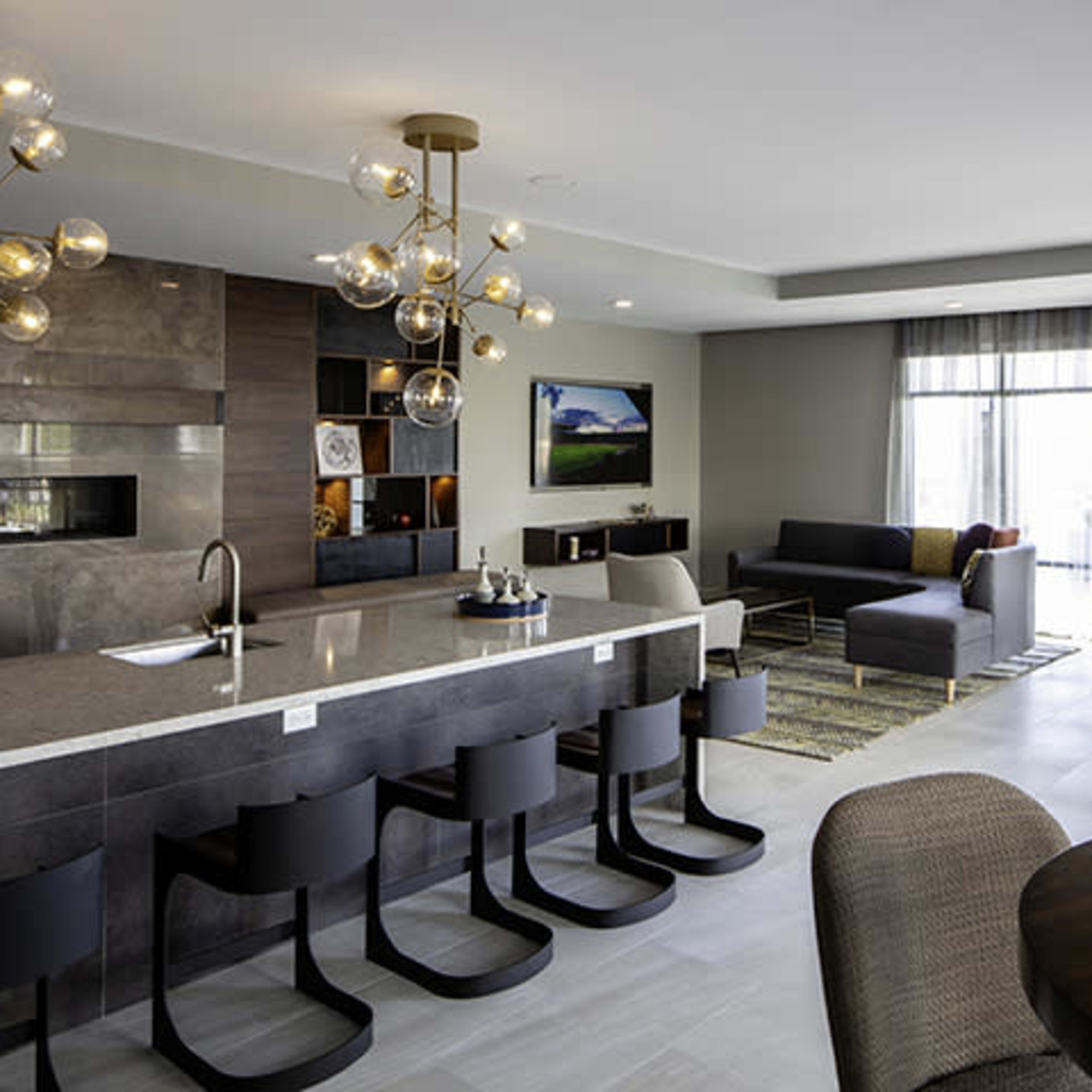 A modern lounge area with a sleek kitchen island, bar stools, comfortable seating, and large windows allowing natural light.
